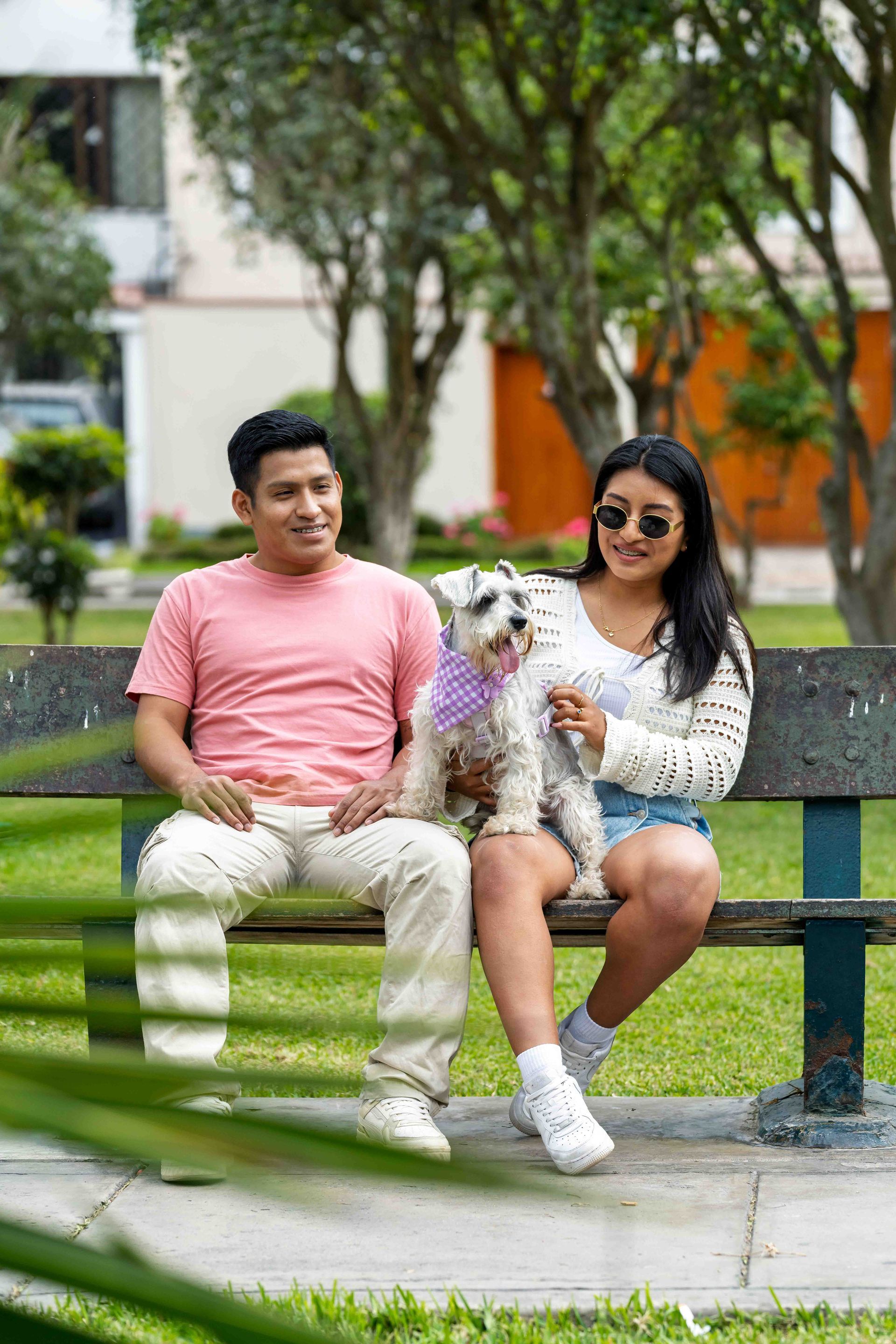 Man and woman sitting on park bench, talking. Sunny day, man looking at woman, woman holding purse.