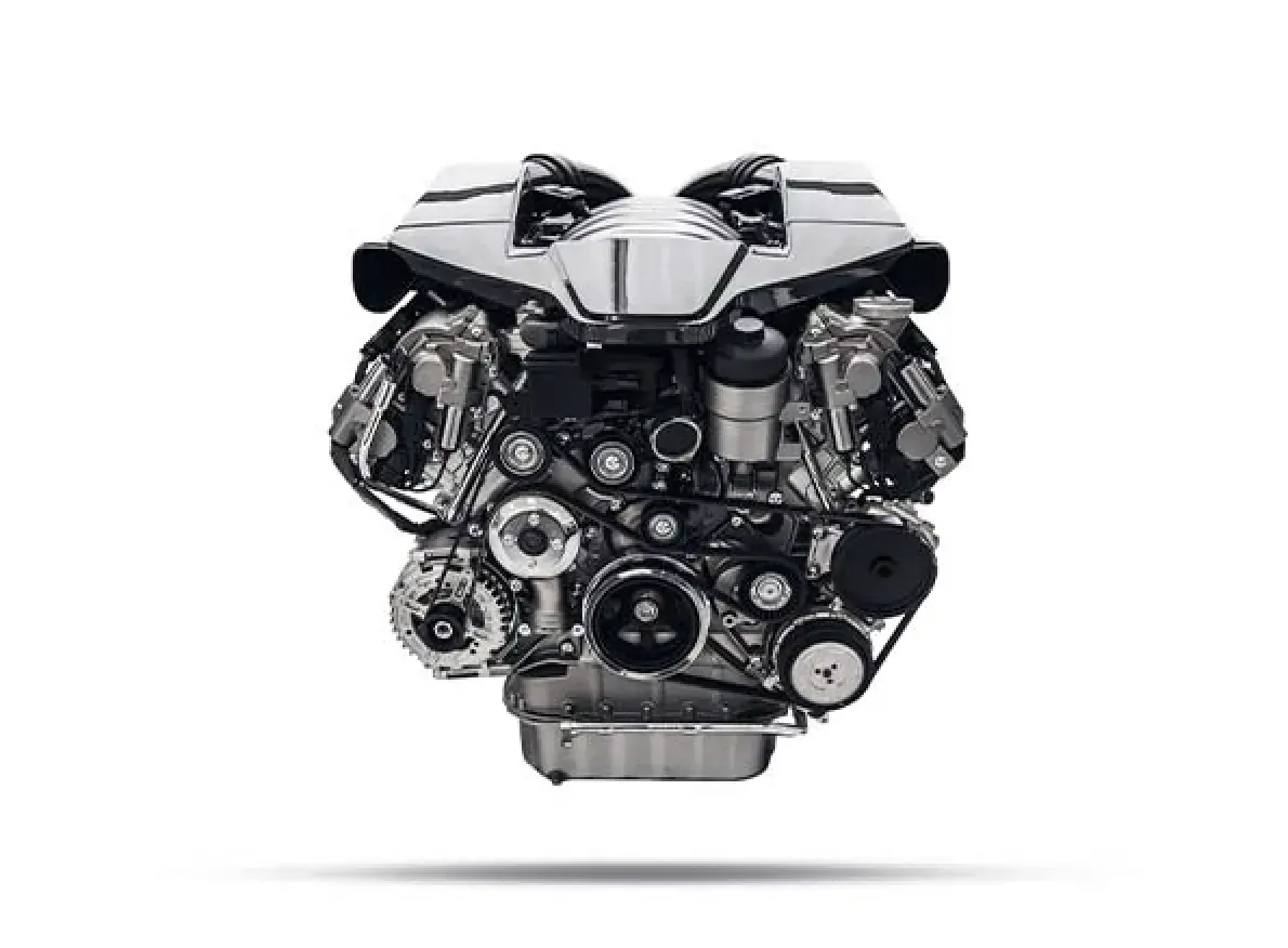 Motor prateado contra um fundo branco; peças mecânicas visíveis, incluindo correias e polias.