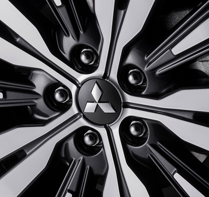 Detalhe da roda de um carro Mitsubishi. Design em preto e prata com o logotipo da Mitsubishi ao centro.