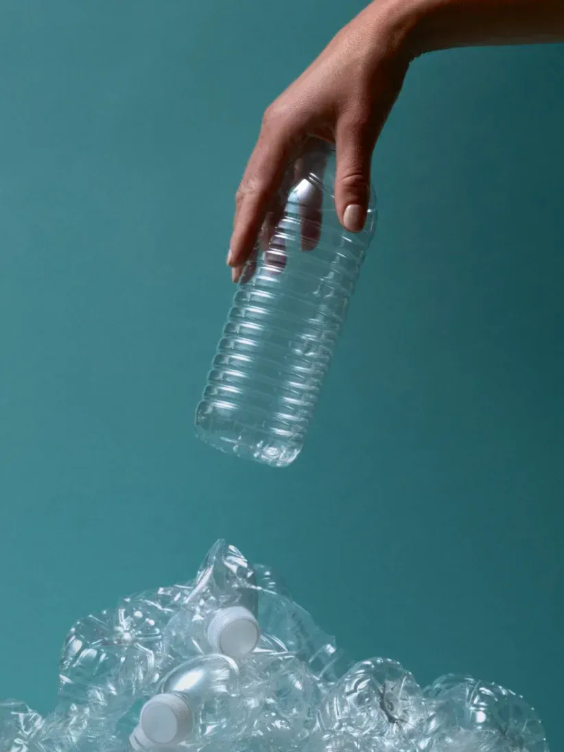 A person is throwing a plastic bottle into a pile of plastic bottles.
