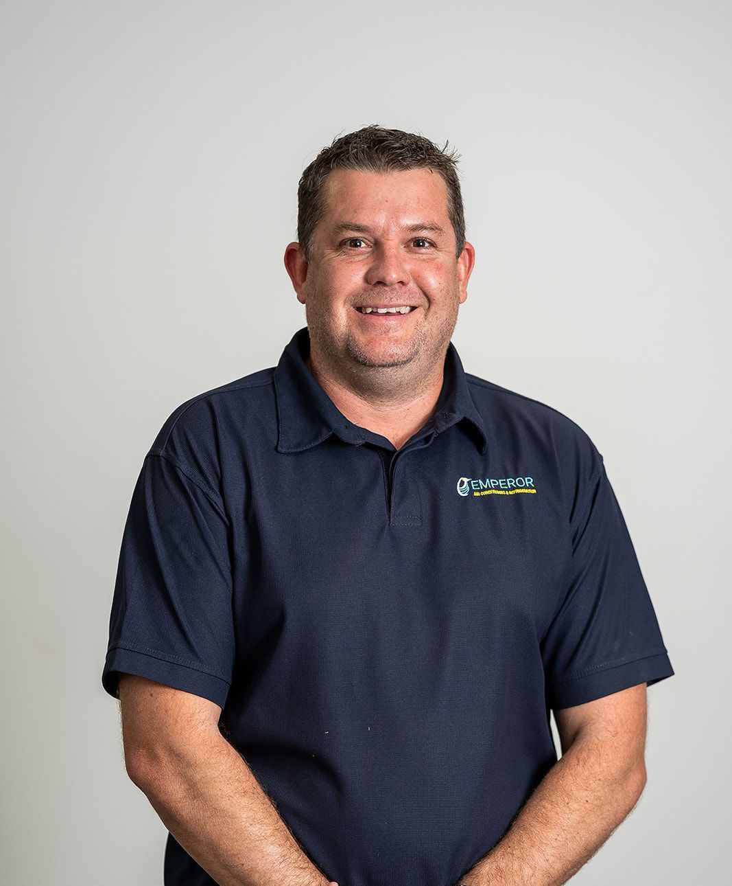 Man in a navy blue polo shirt smiles, posing against a white background.