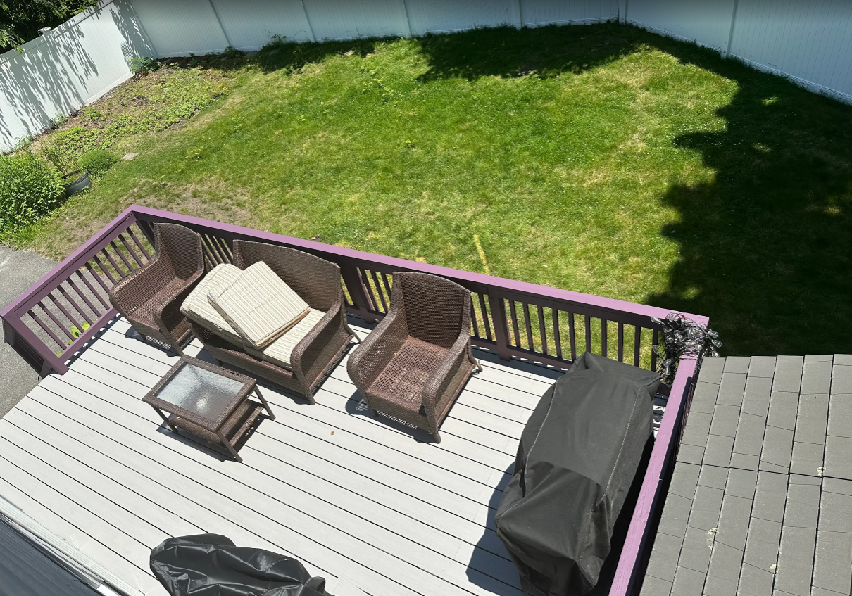 Wooden deck with wicker furniture, grill, and a grassy yard.