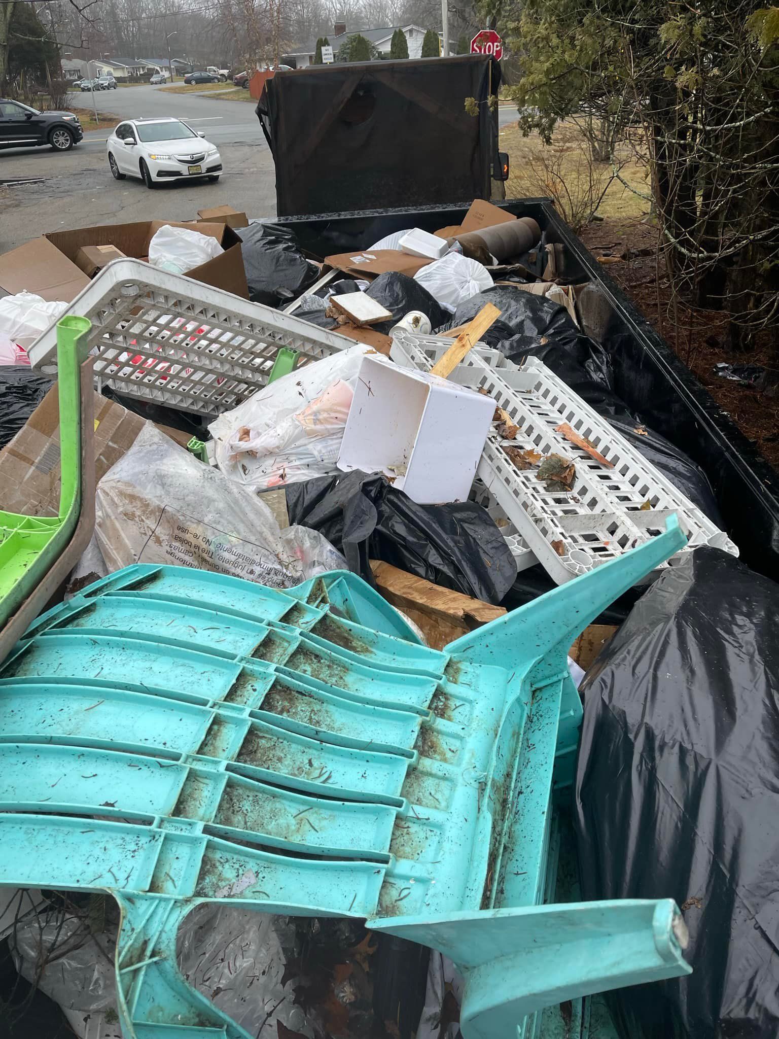 A dumpster filled with trash, including a green and blue plastic chair, and other debris in an outdoor setting.