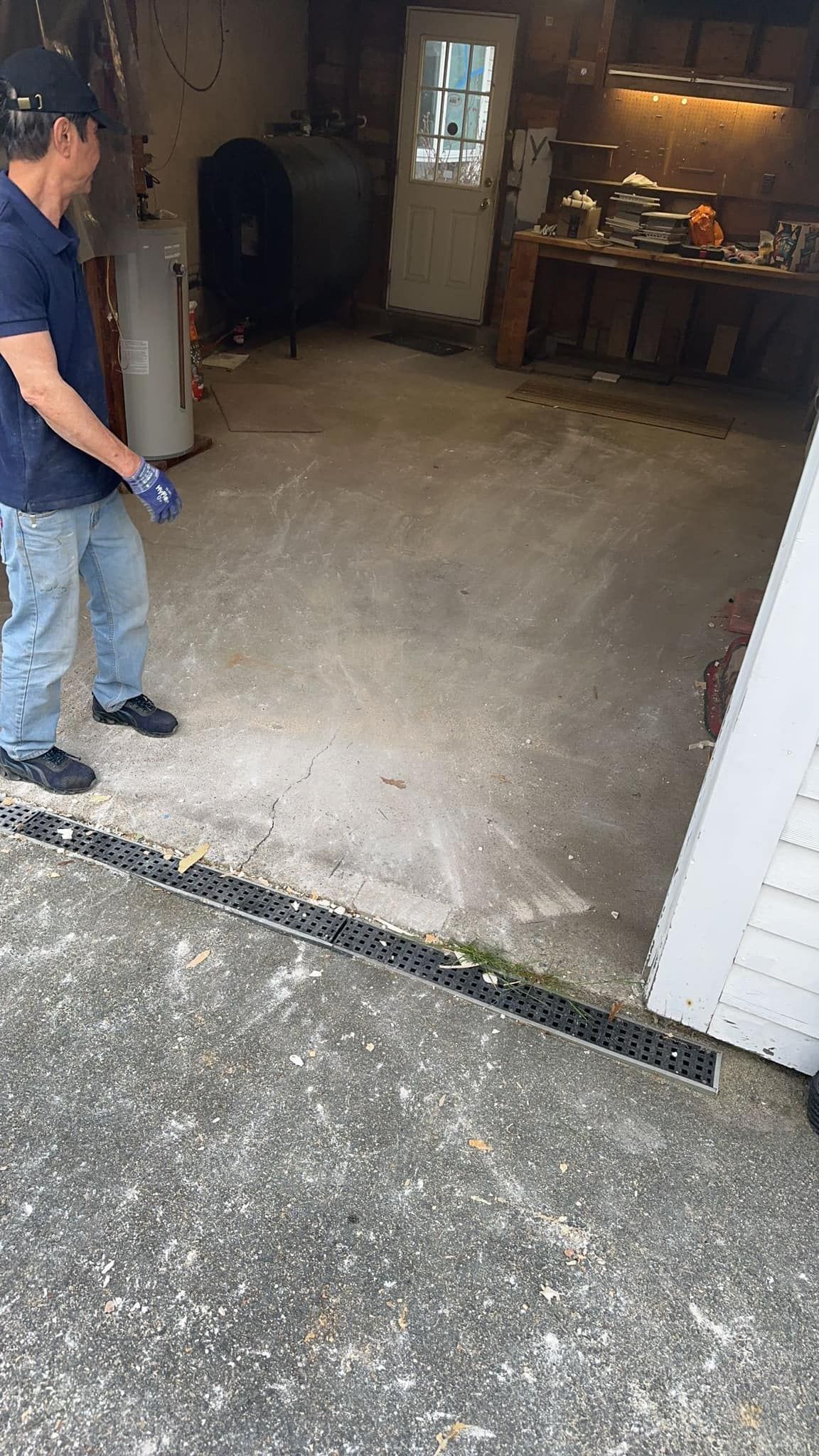Man in garage with water heater, dark tank, and open door.