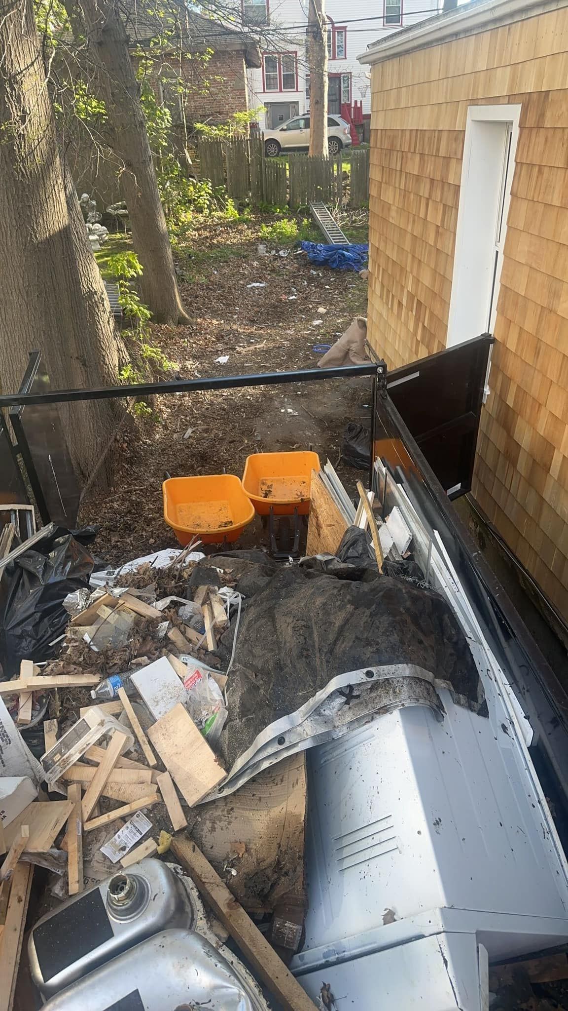 Overgrown yard with trash, two orange chairs, and part of a building with wood shingle siding.
