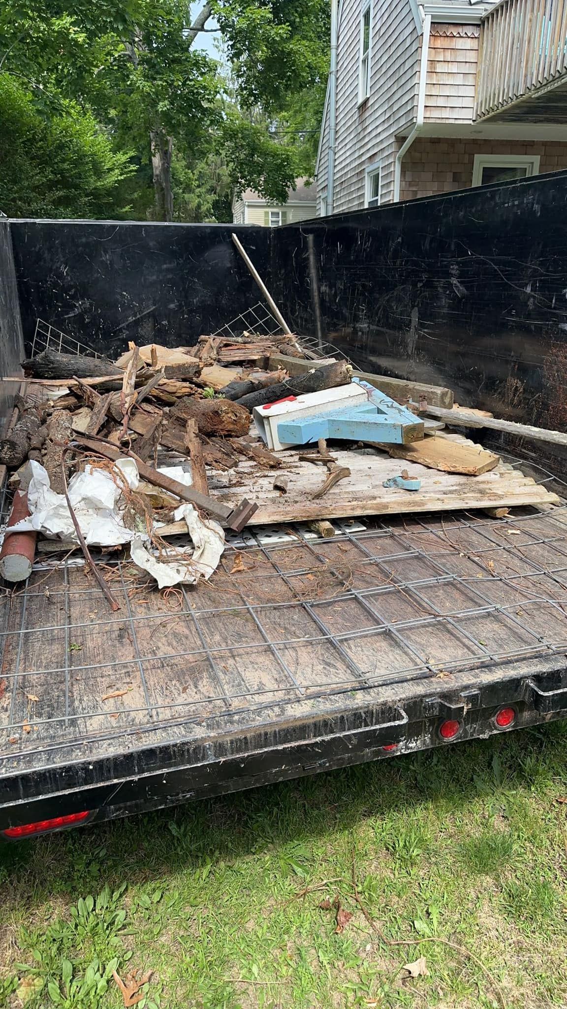 Dumpster filled with construction debris on a trailer, set on grass, with building and trees in background.