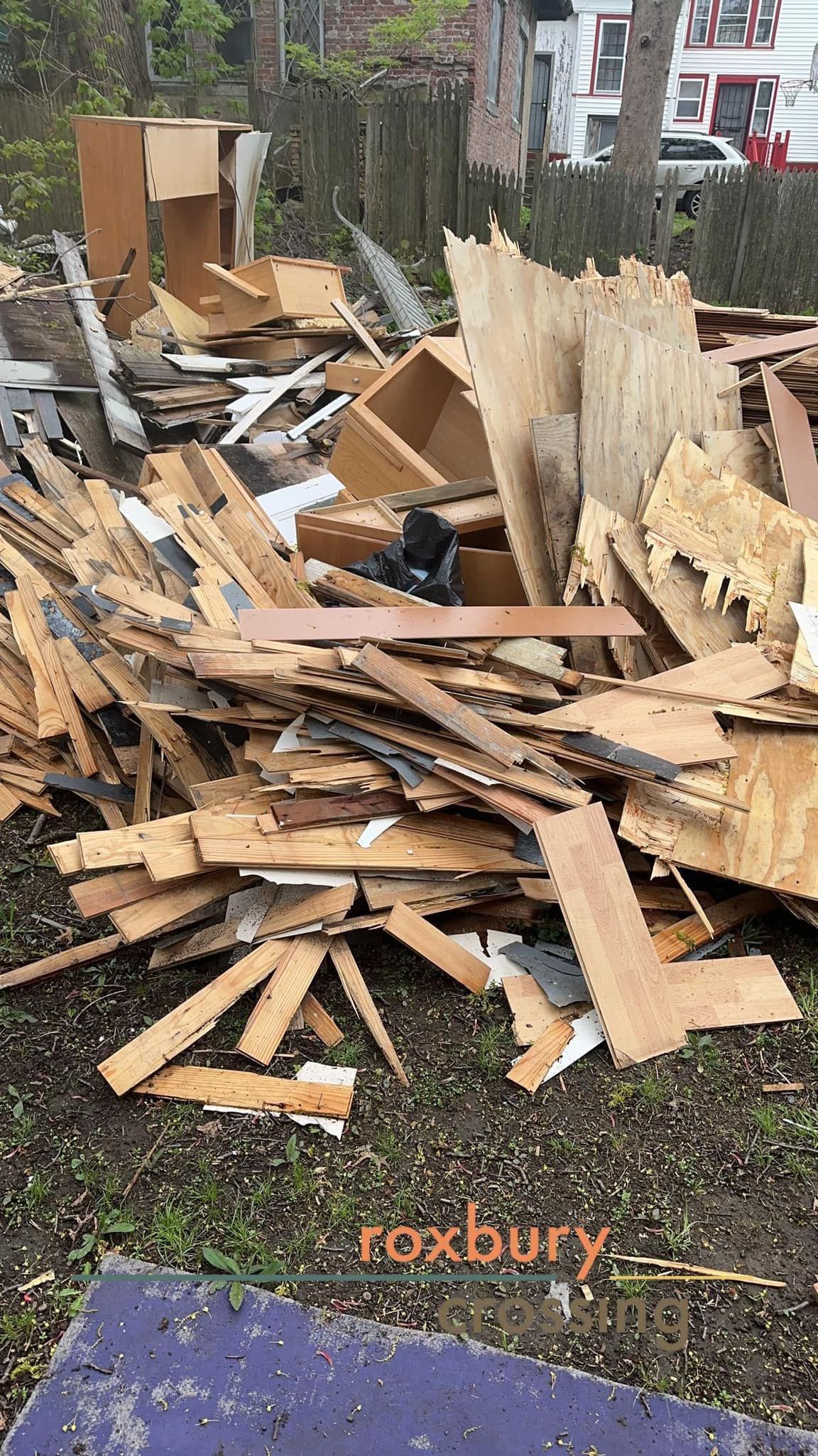 Pile of construction debris outdoors: wood, particleboard, and cabinets.