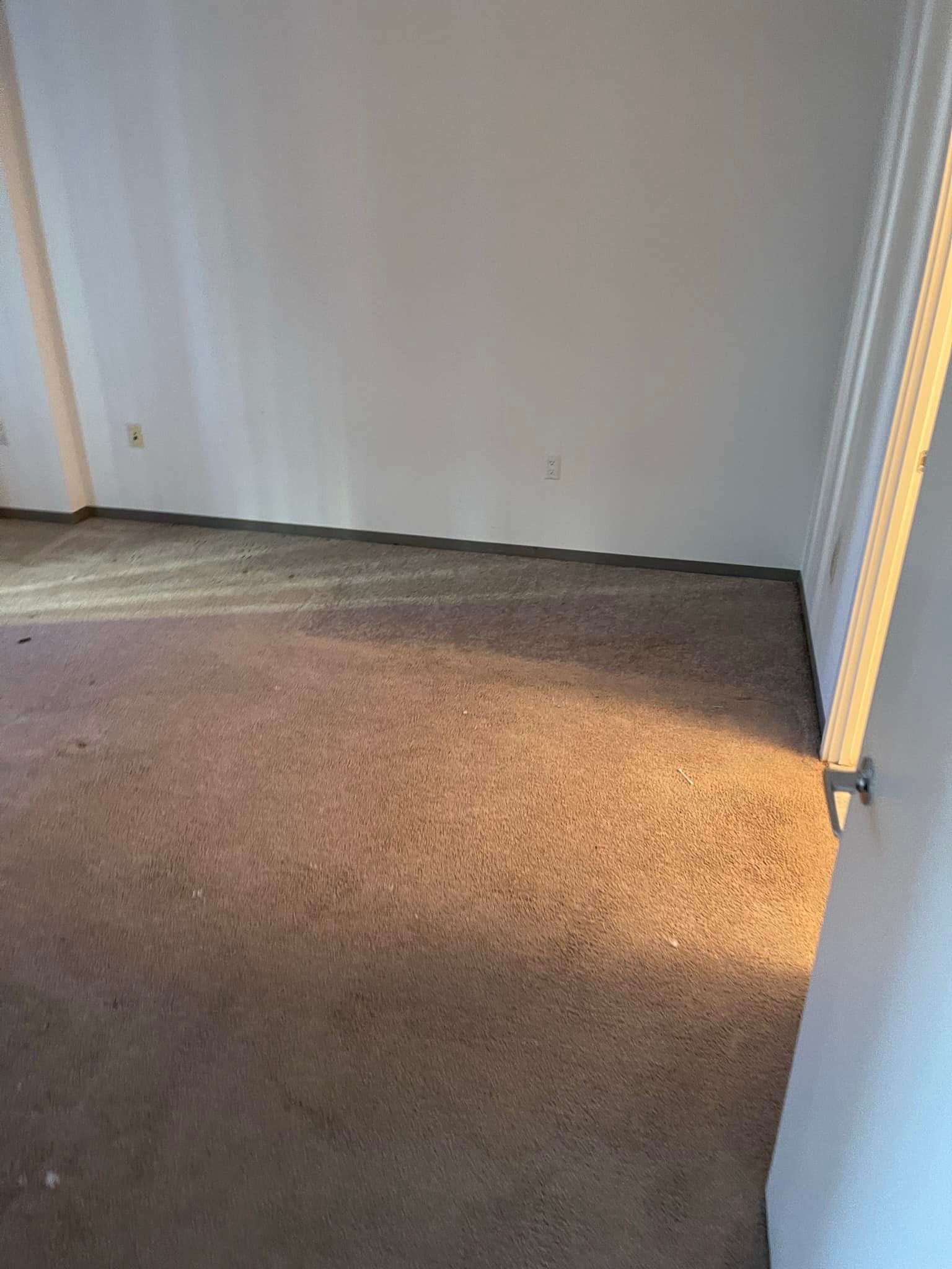Empty room with stained brown carpet and white walls, door on the right.