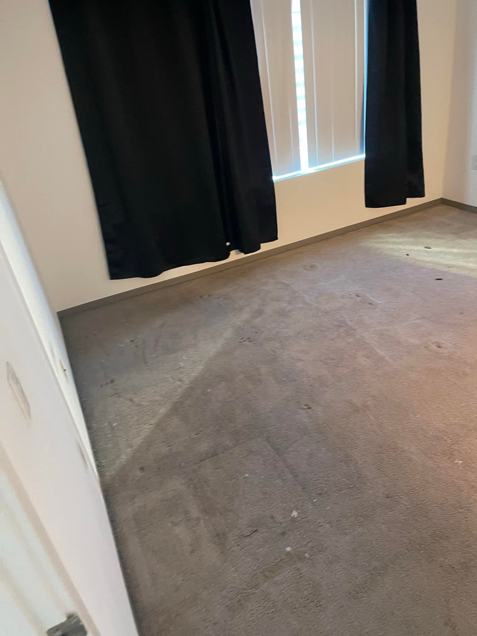 Gray carpeted room with black curtains over a window.