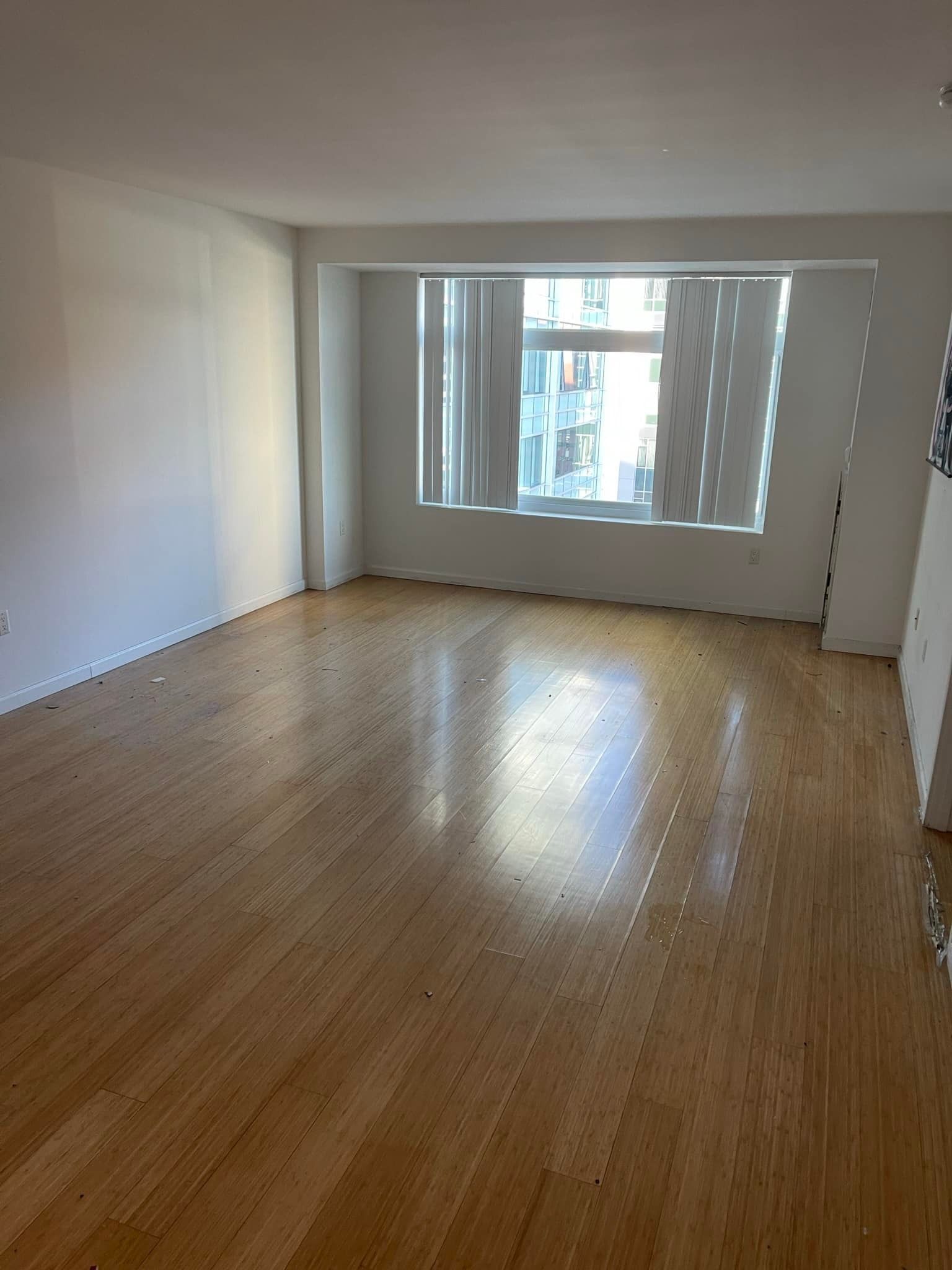 Empty room with hardwood floors, white walls, and a window with blinds.