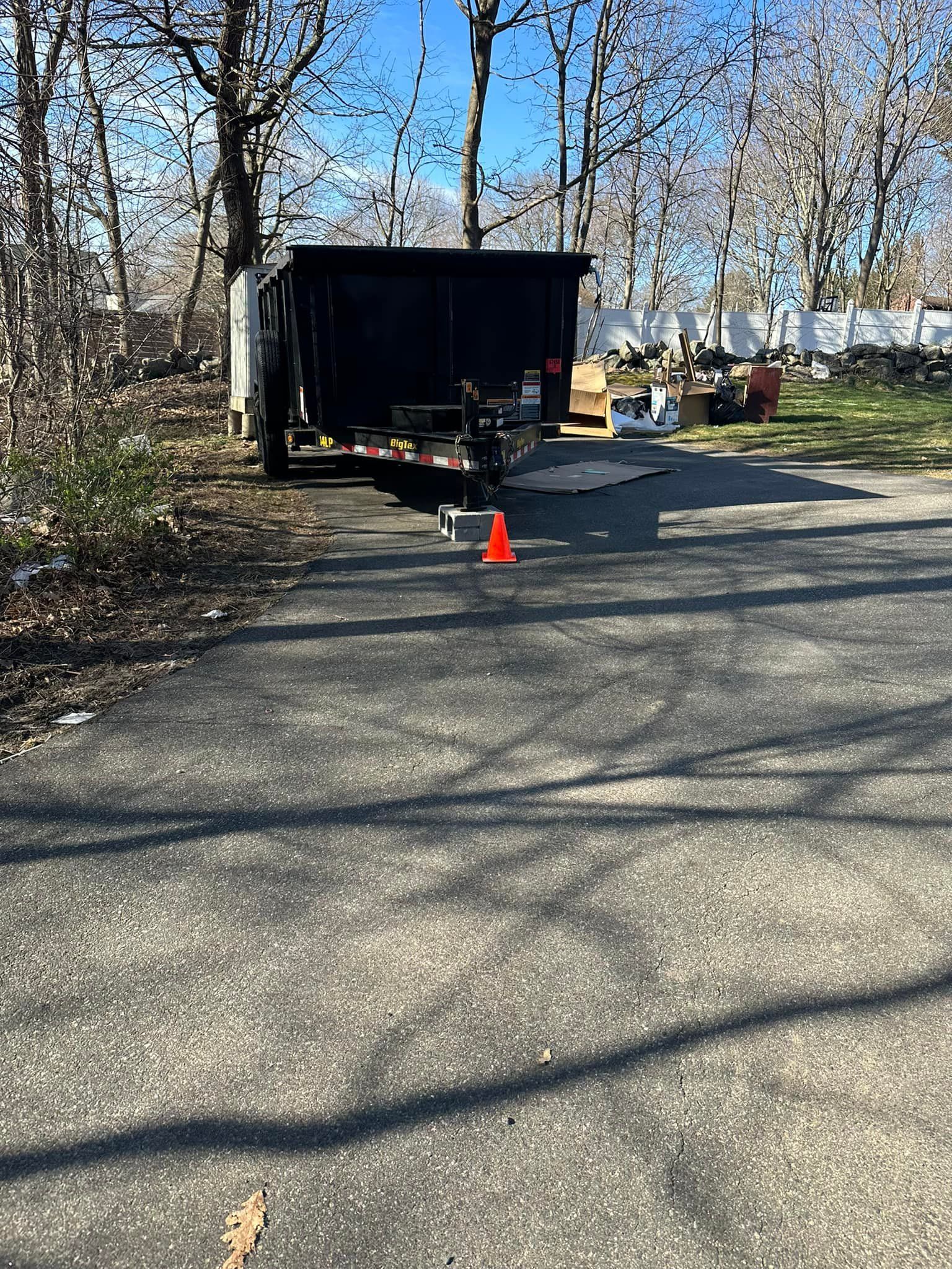 Dumpster trailer in driveway with debris and an orange cone.