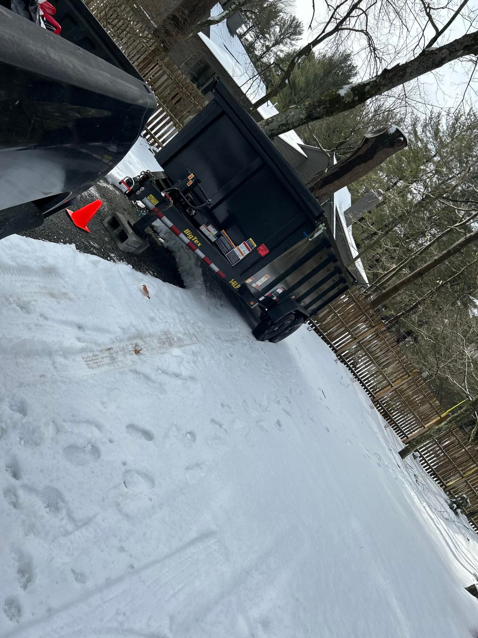 Dump truck on snowy ground, angled slightly, with orange cone visible.