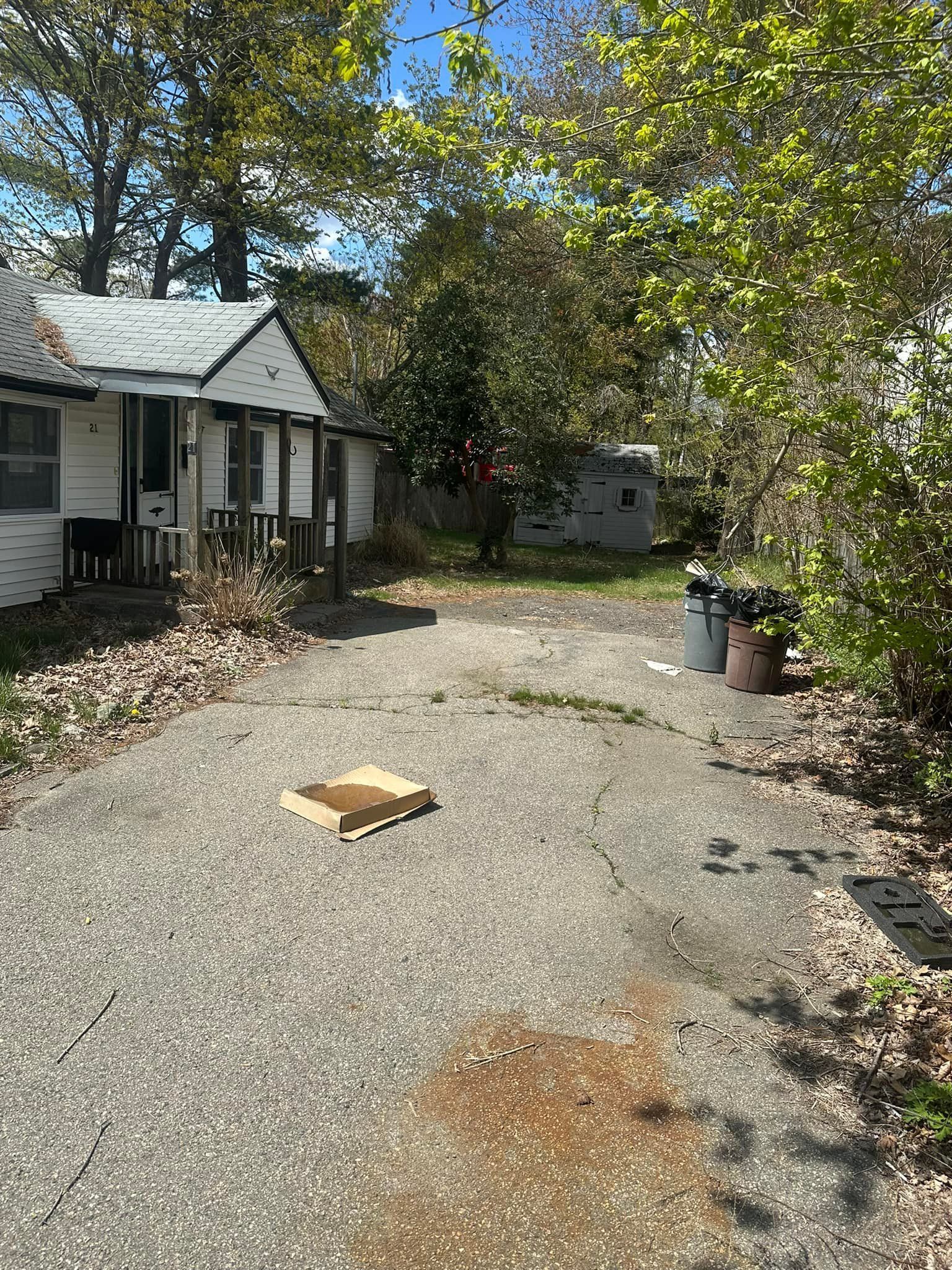 Cracked driveway leading to a small white house with porch, surrounded by trees.