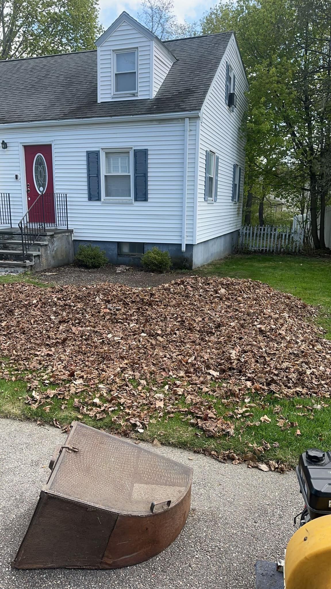 A house with a large pile of leaves on the front lawn, a leaf blower in the foreground.