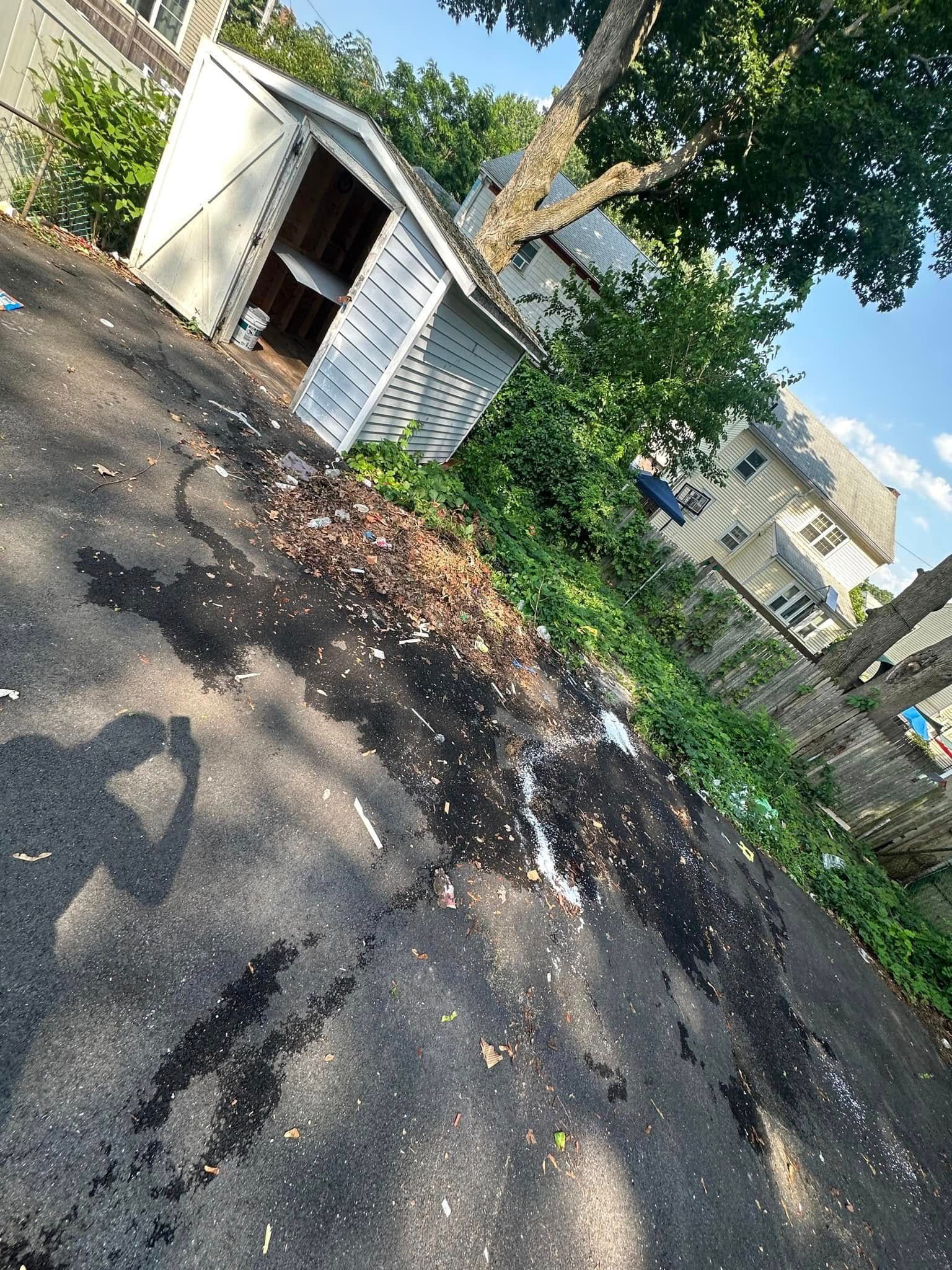 Backyard with shed, blacktop, leaves, and sunlight. Shadow of a person taking a photo.