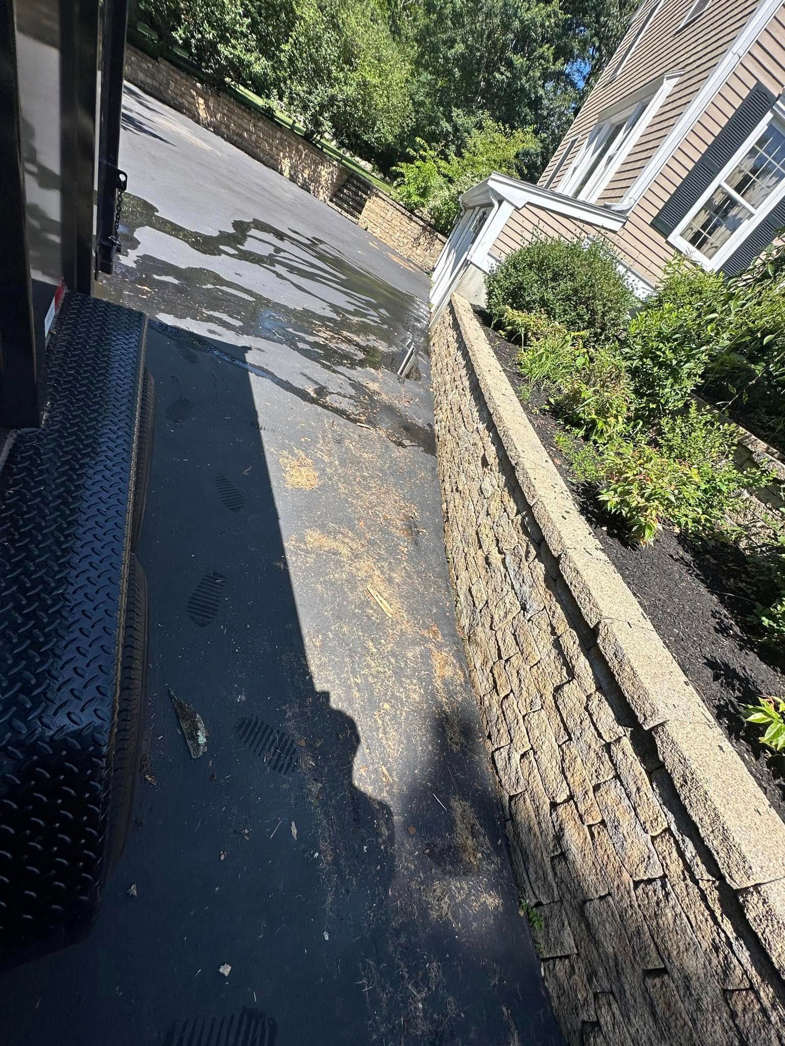 A black, textured surface covered in debris; a concrete retaining wall and house in the background.