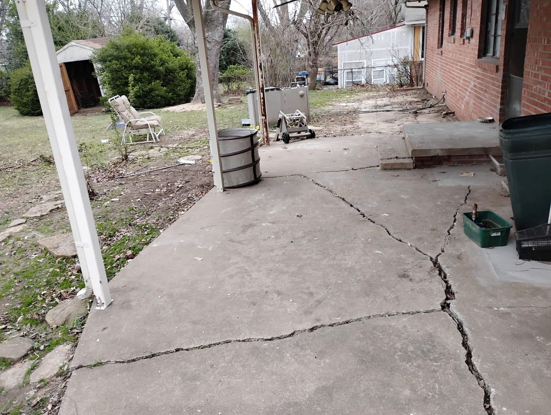 Cracked concrete patio next to a brick building and overgrown yard.