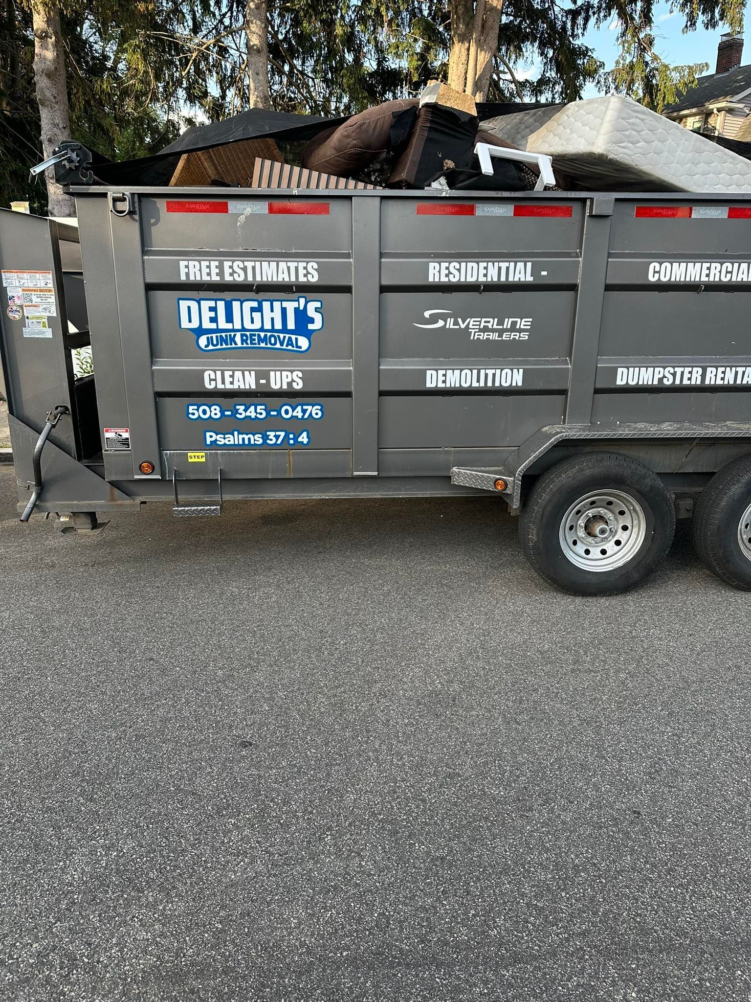 Gray dumpster filled with debris; Delight's Dumpsters logo on side, parked on gravel.