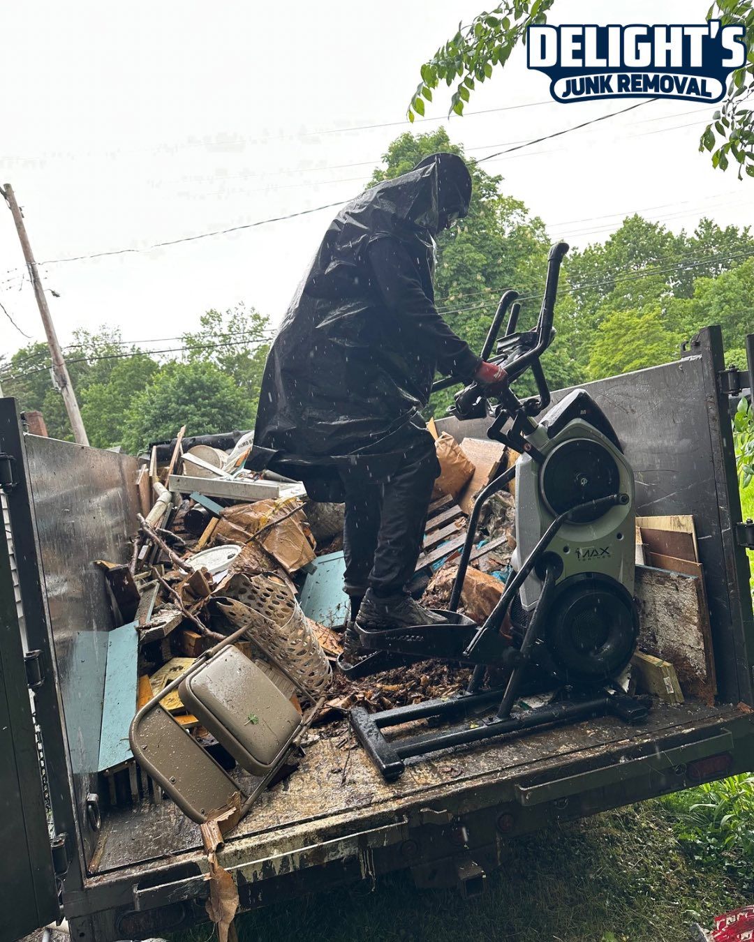 Person in raincoat loads junk into a truck. Includes old exercise machine and wood.