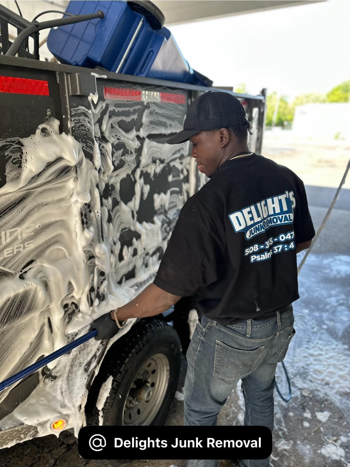 Man in black shirt cleaning a trailer with soap and brush.