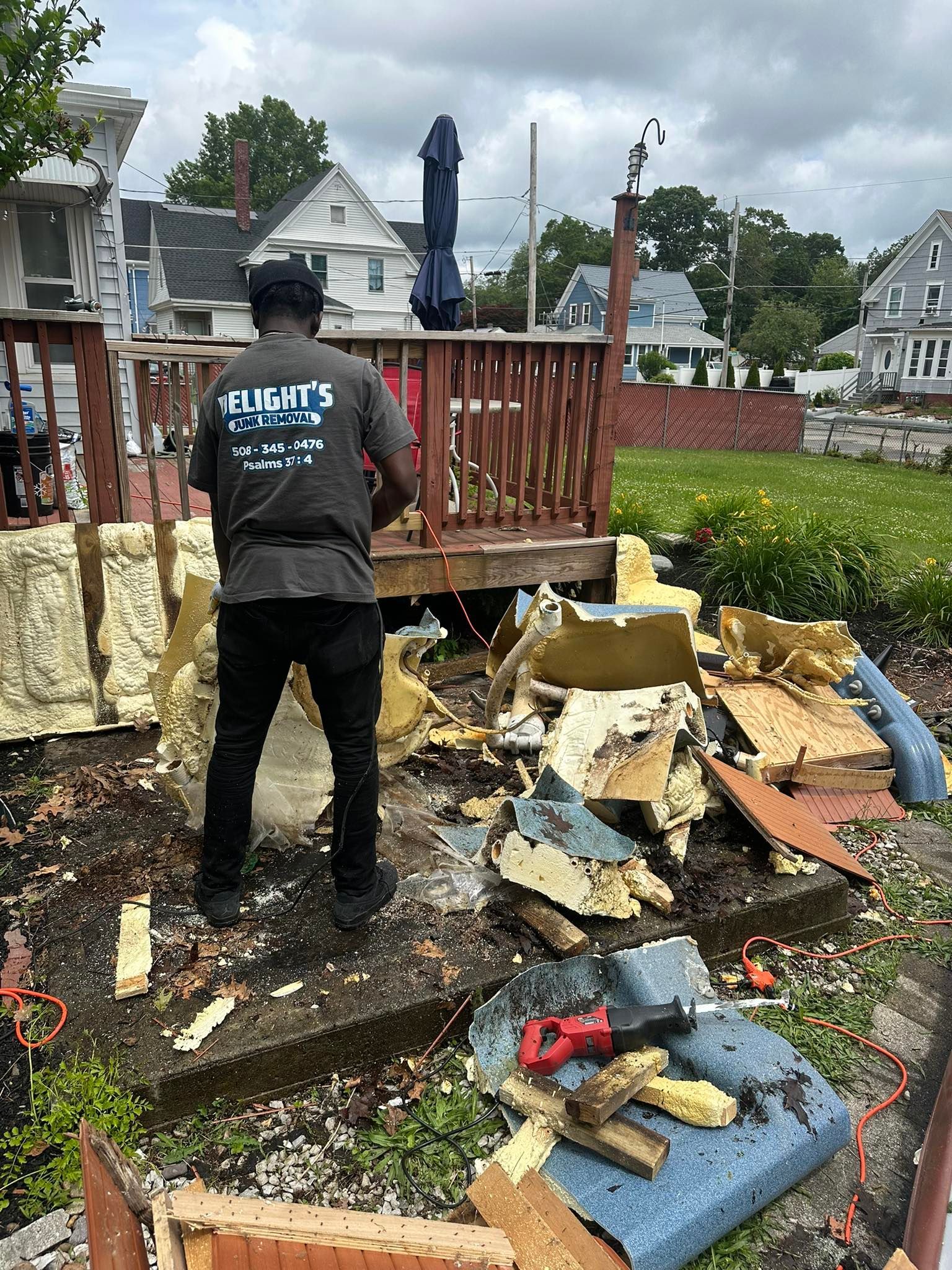 A man tears up deck with rubble in front of the house on a cloudy day.