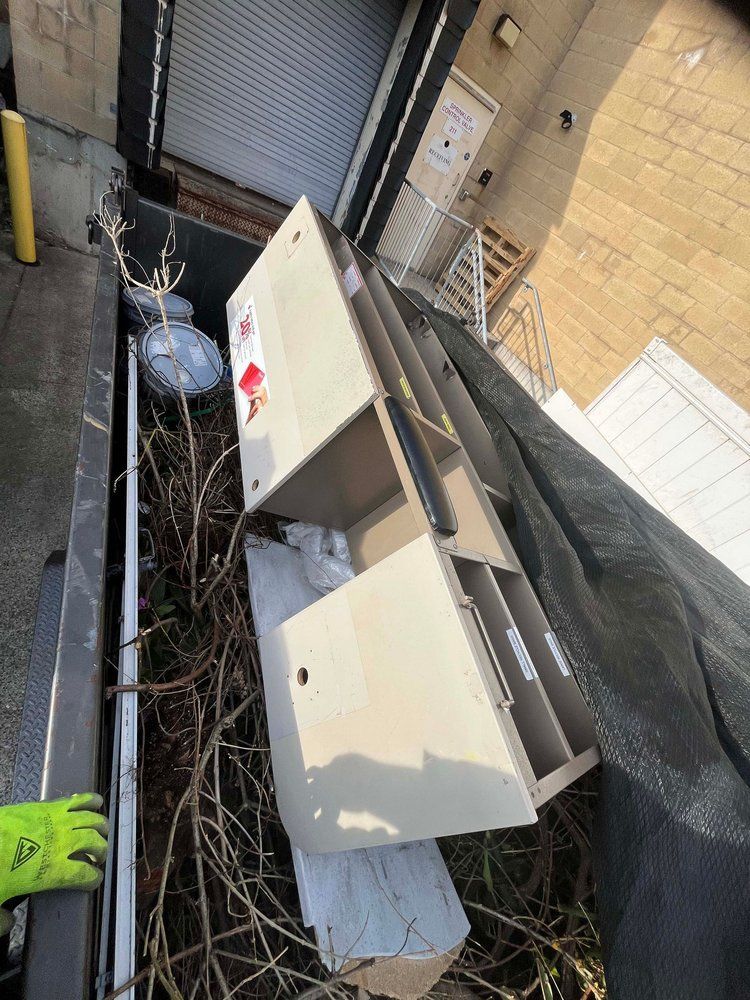 An office cabinet laying on its side in an outdoor space with debris and a partly visible building.