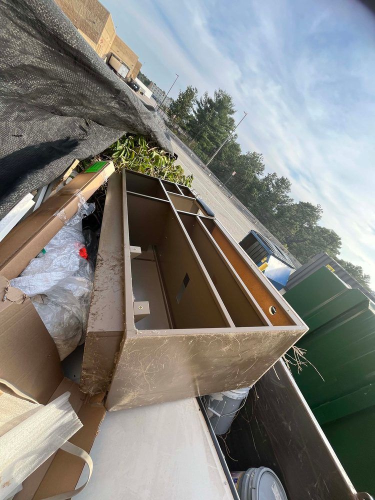 Brown, open-topped container in a dumpster, surrounded by trash and debris.