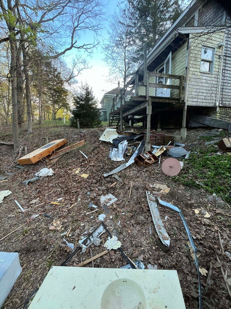 Debris strewn yard with weathered house, deck, and trees. Mostly brown, white, and gray colors.