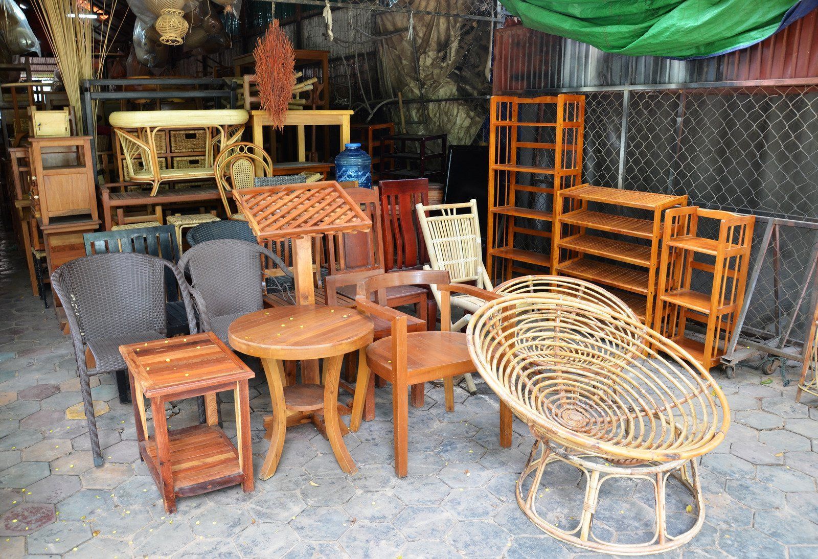 Wooden furniture displayed outside: chairs, tables, shelves, and a large woven chair.