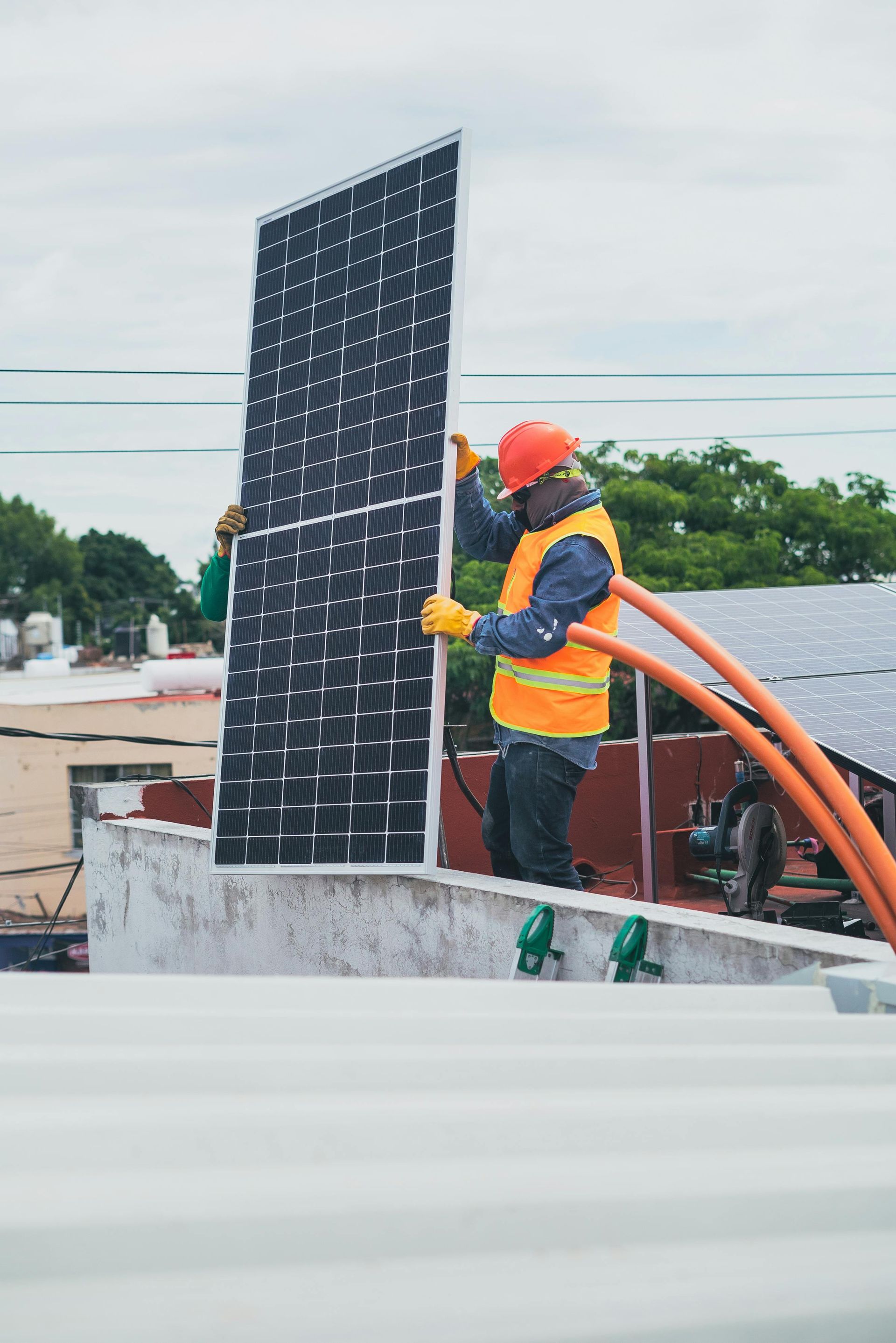 Solar panel installer on a rooftop wearing safety gear, holding a panel.