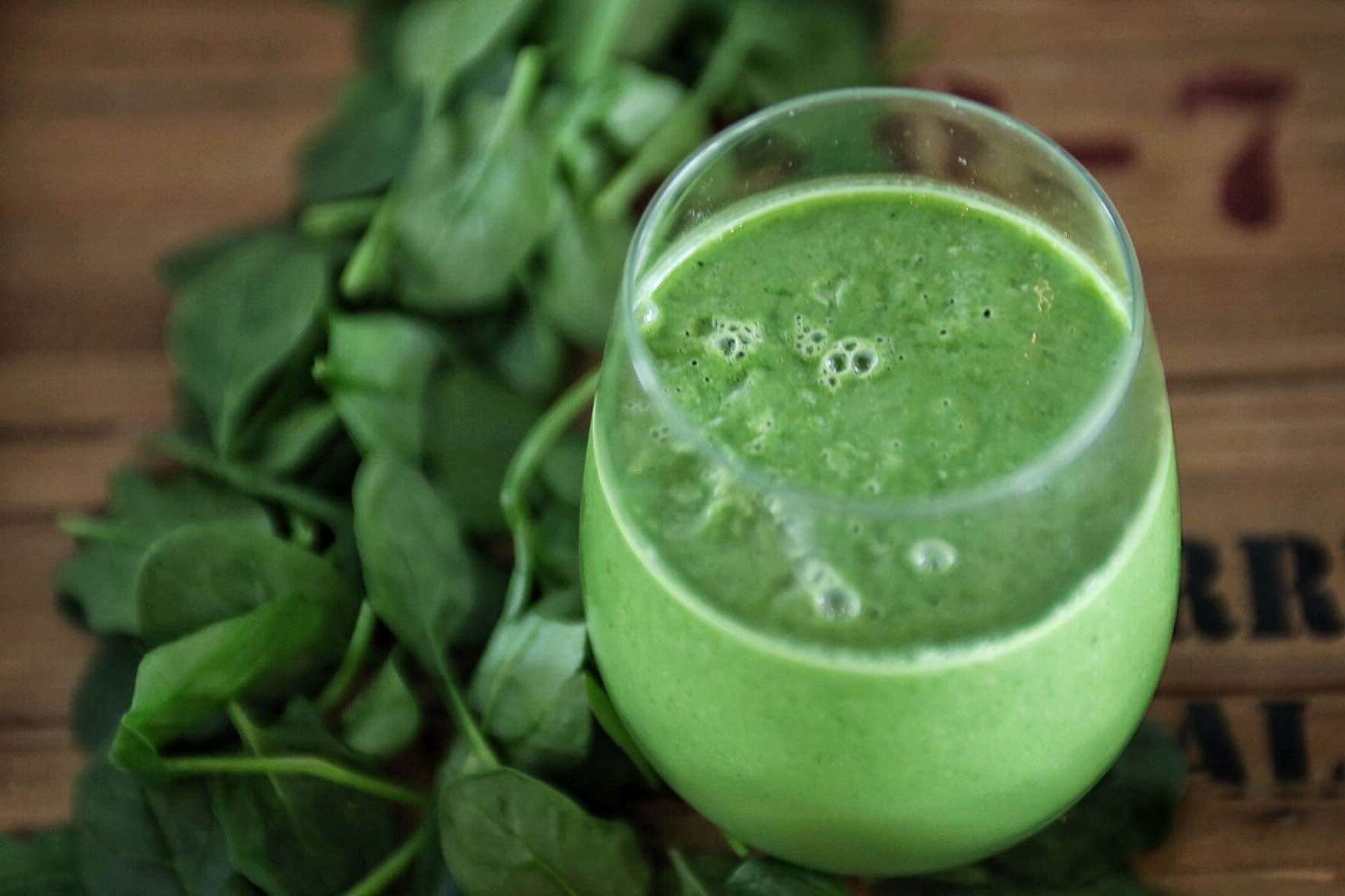 A close up of a green smoothie in a glass on a table.