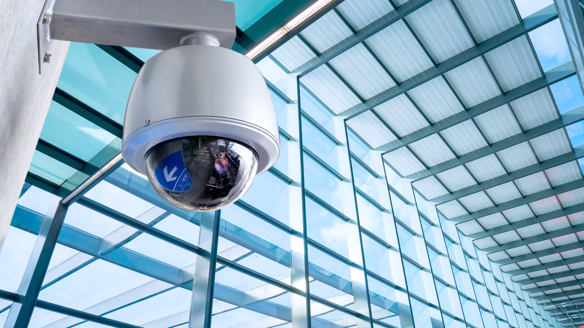 Security camera mounted on a wall in a modern building with a glass ceiling.