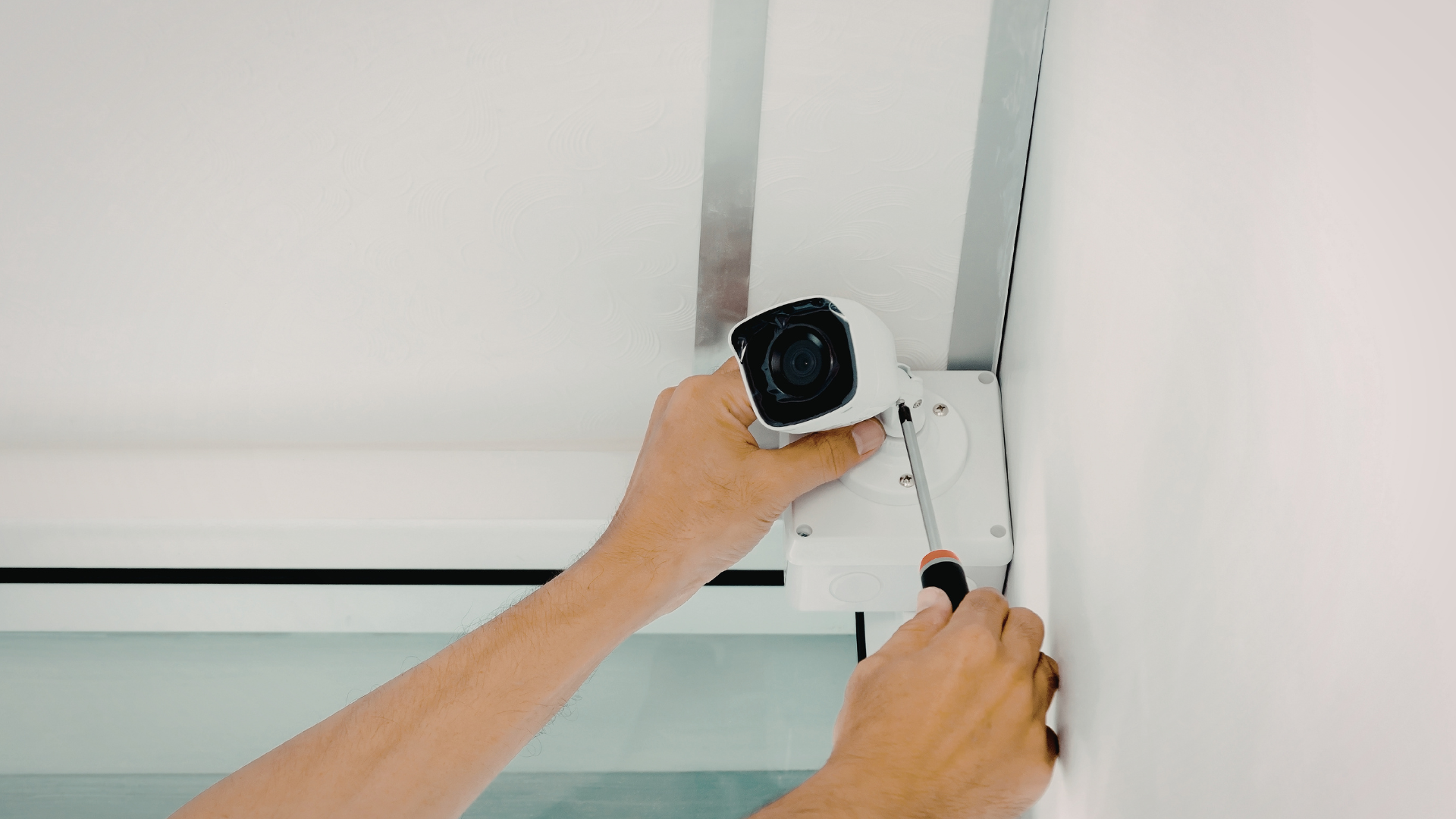 Person installing a security camera on a white wall using a screwdriver.