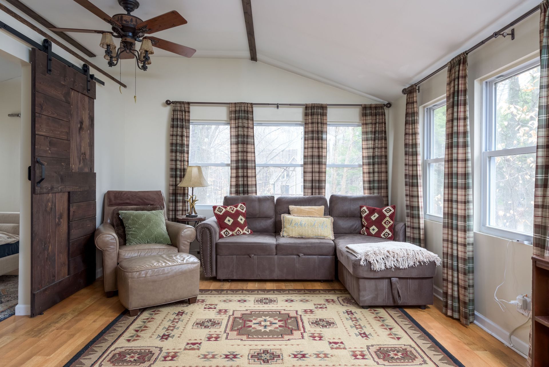 A living room with a couch , chair , rug and ceiling fan.