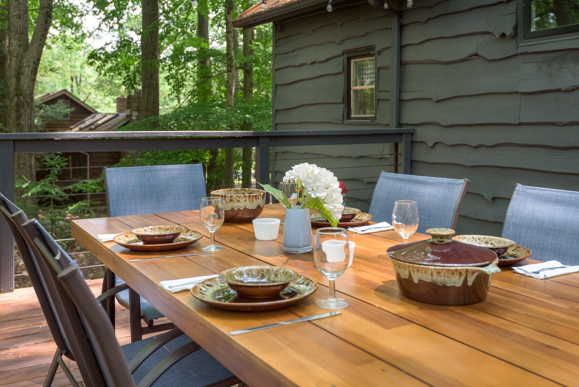 A wooden table with plates , bowls , glasses and a vase of flowers on it.