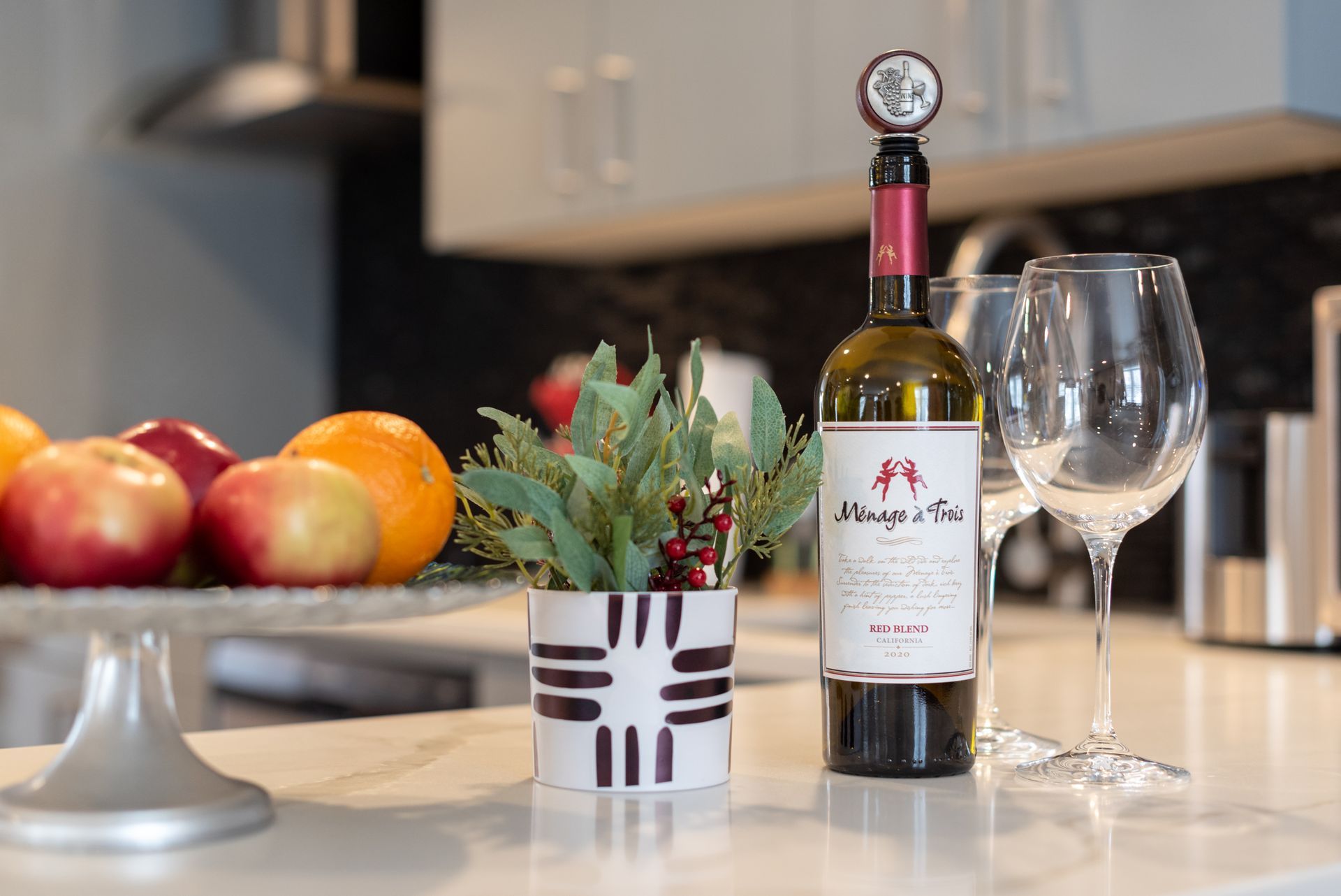 A bottle of wine is sitting on a counter next to two wine glasses.