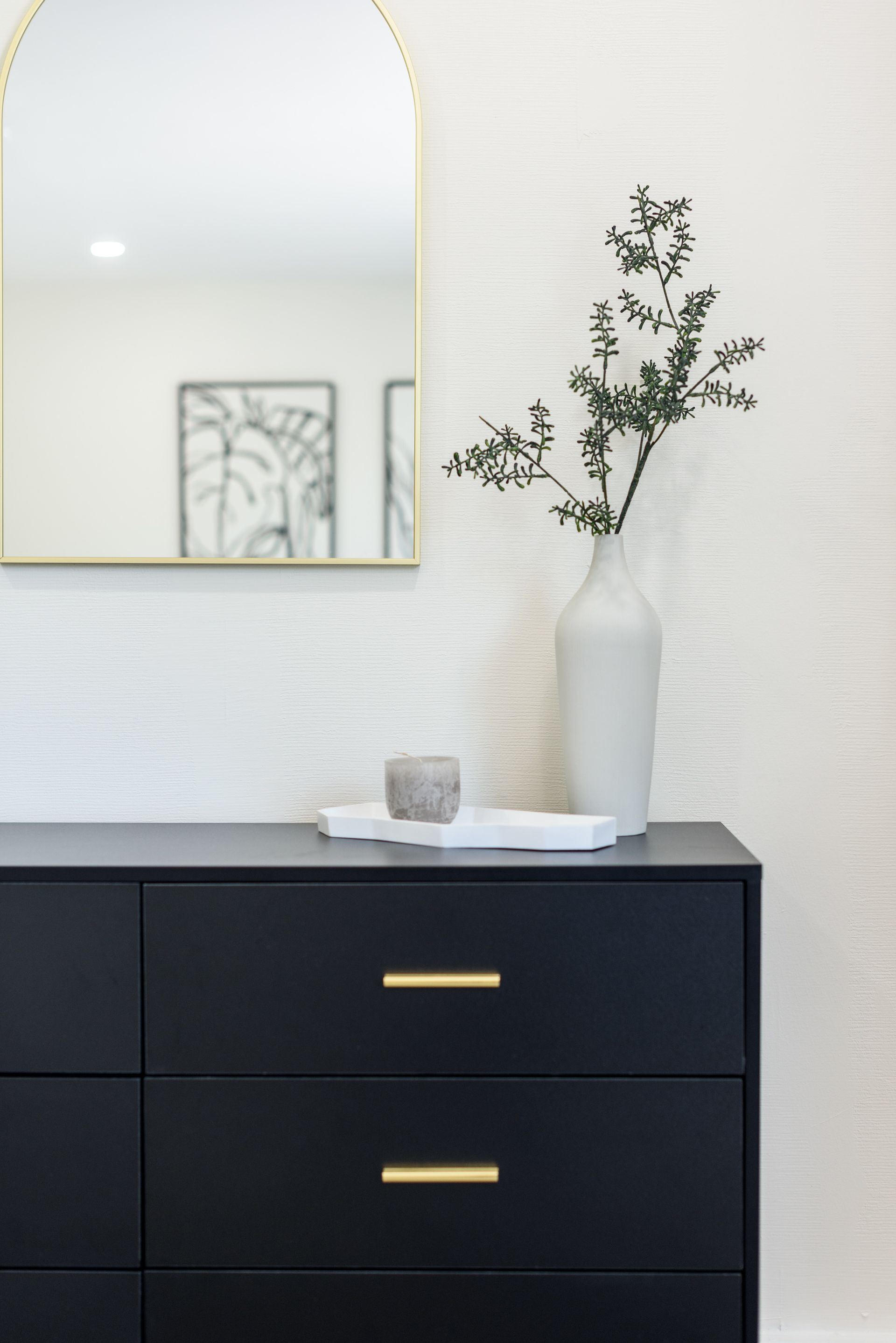 A black dresser with a vase of flowers and a mirror on the wall.