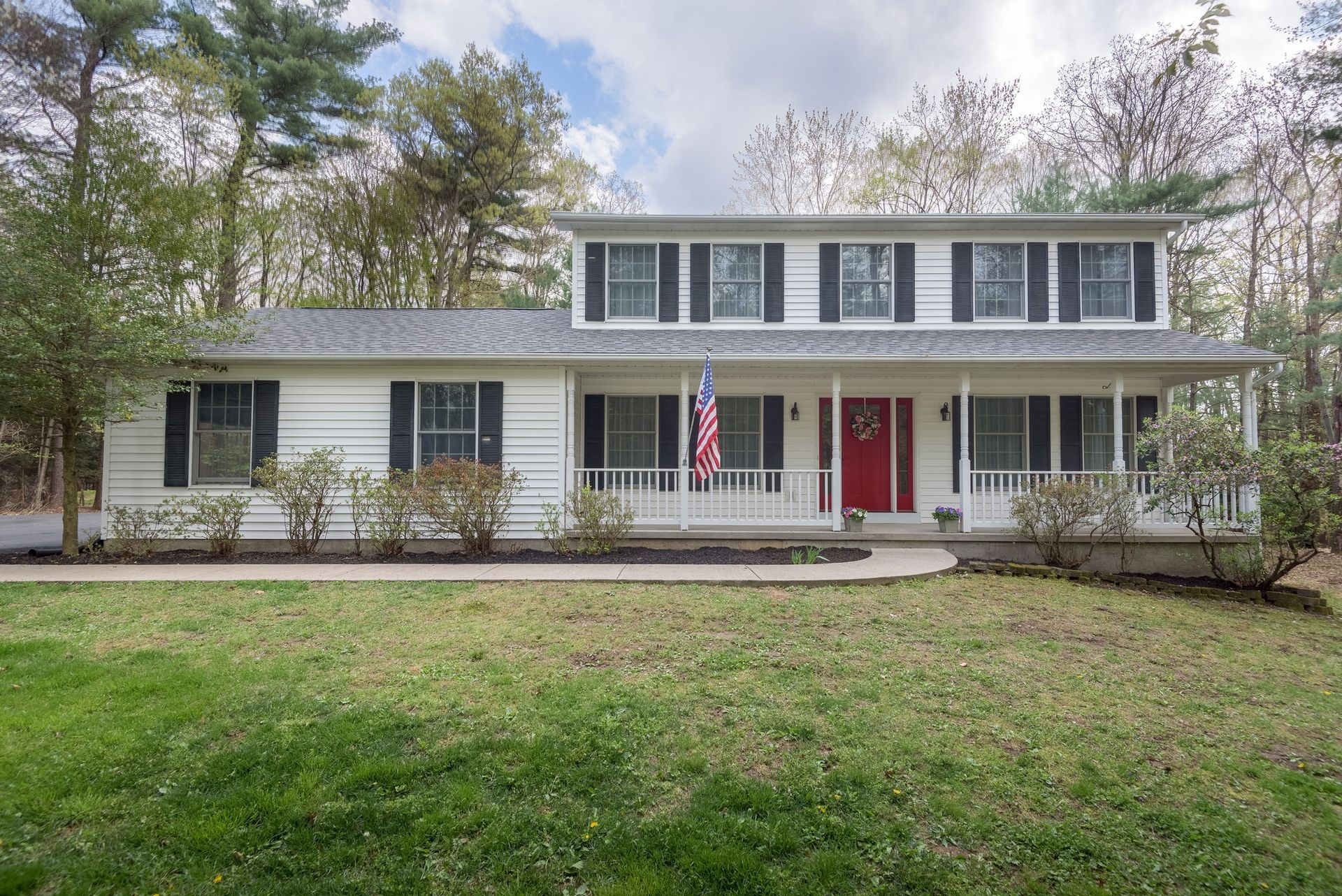 A white house with black shutters and a red door is sitting on top of a lush green lawn.