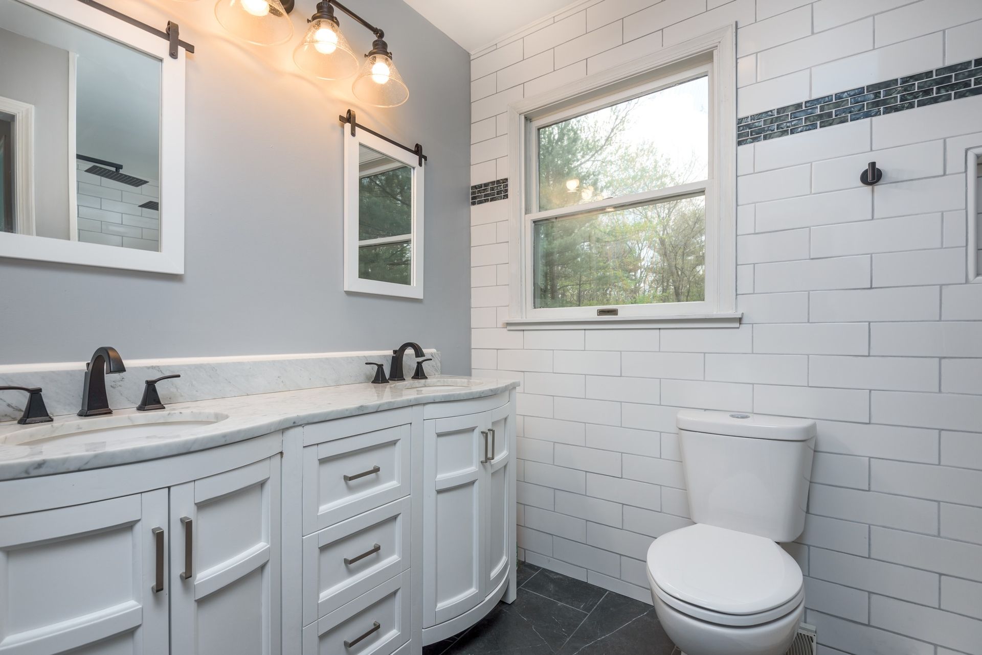 A bathroom with a toilet , sink , mirror and window.