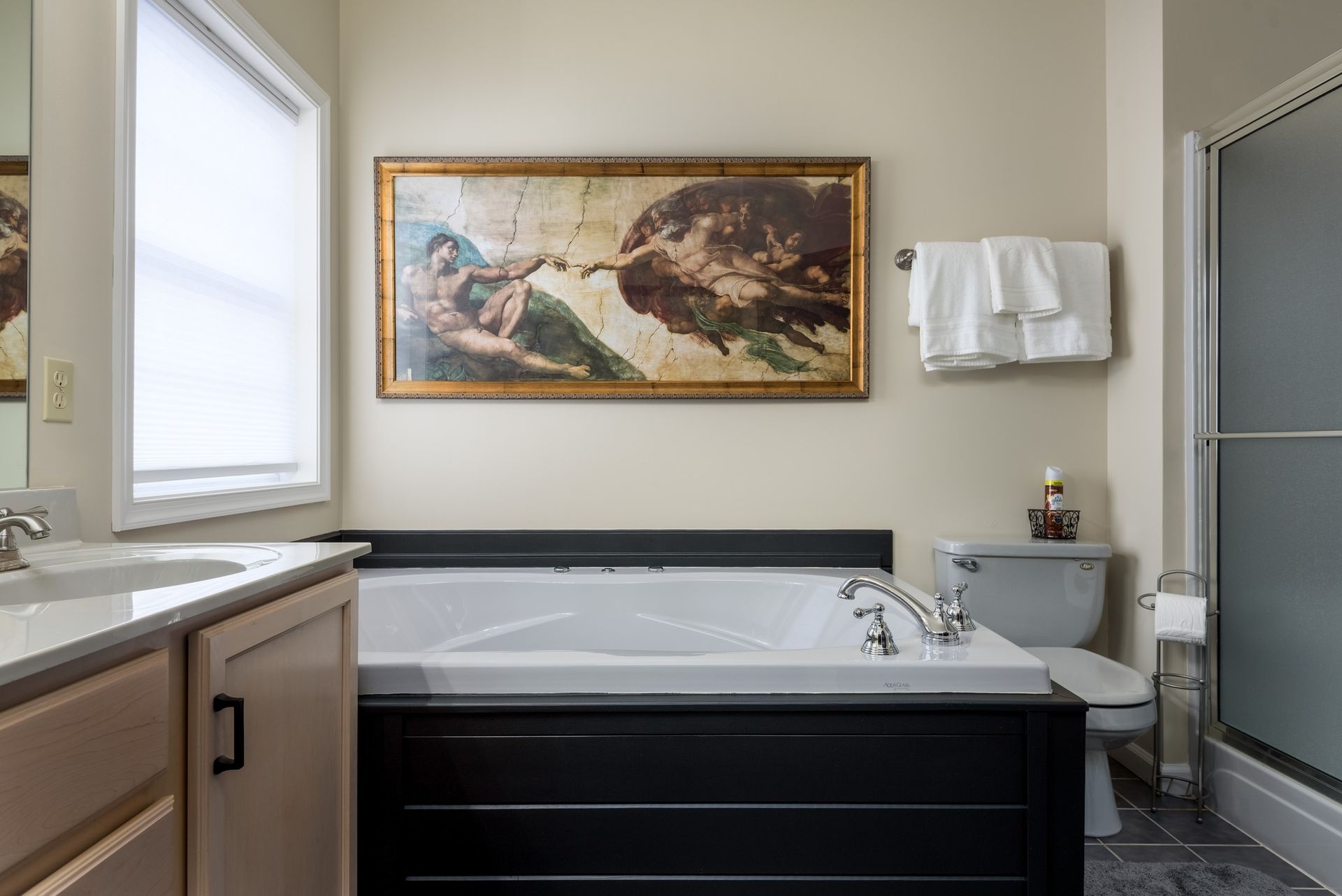 A bathroom with a tub , sink , toilet and a painting on the wall.