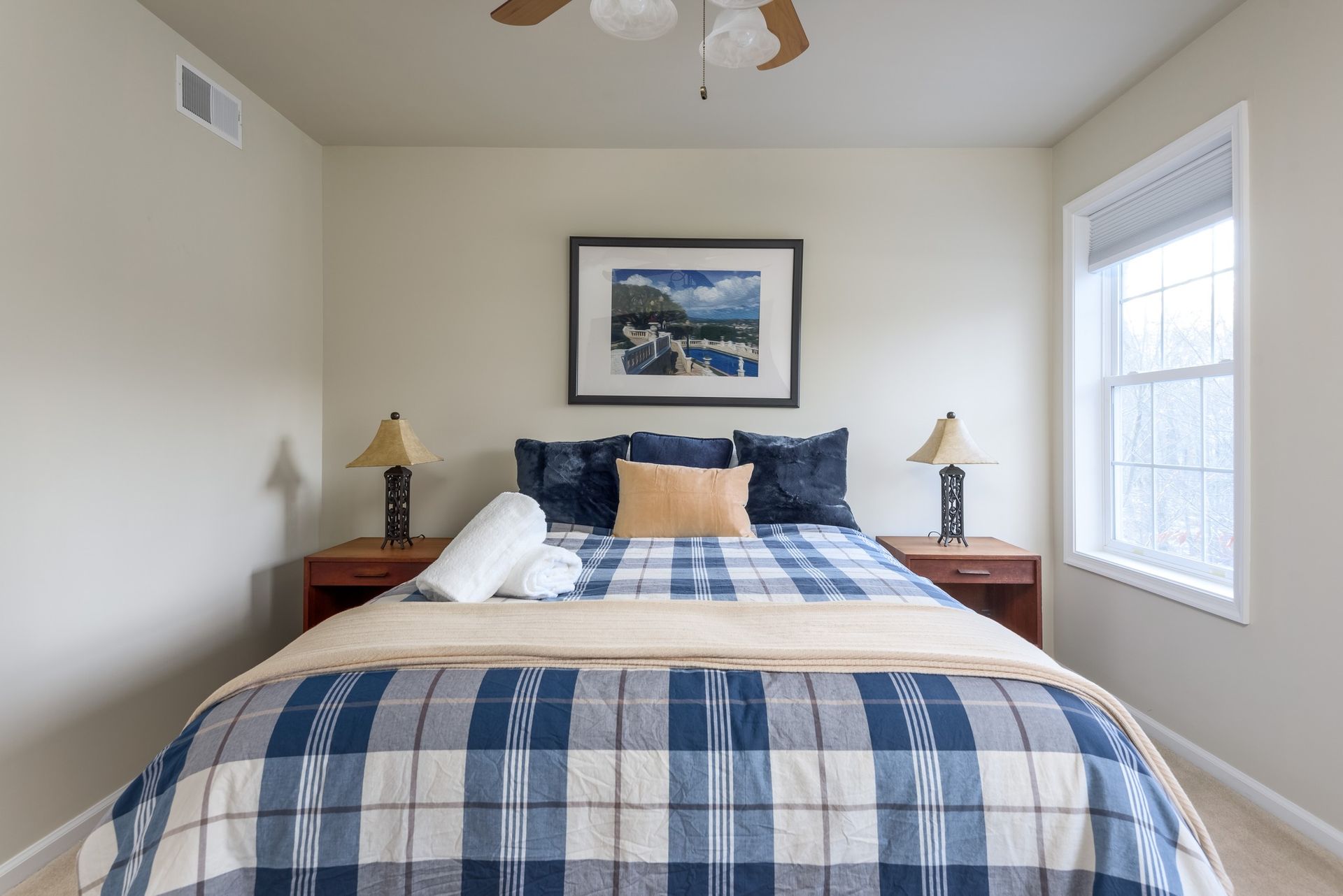 A bedroom with a bed , two lamps , a picture on the wall and a ceiling fan.
