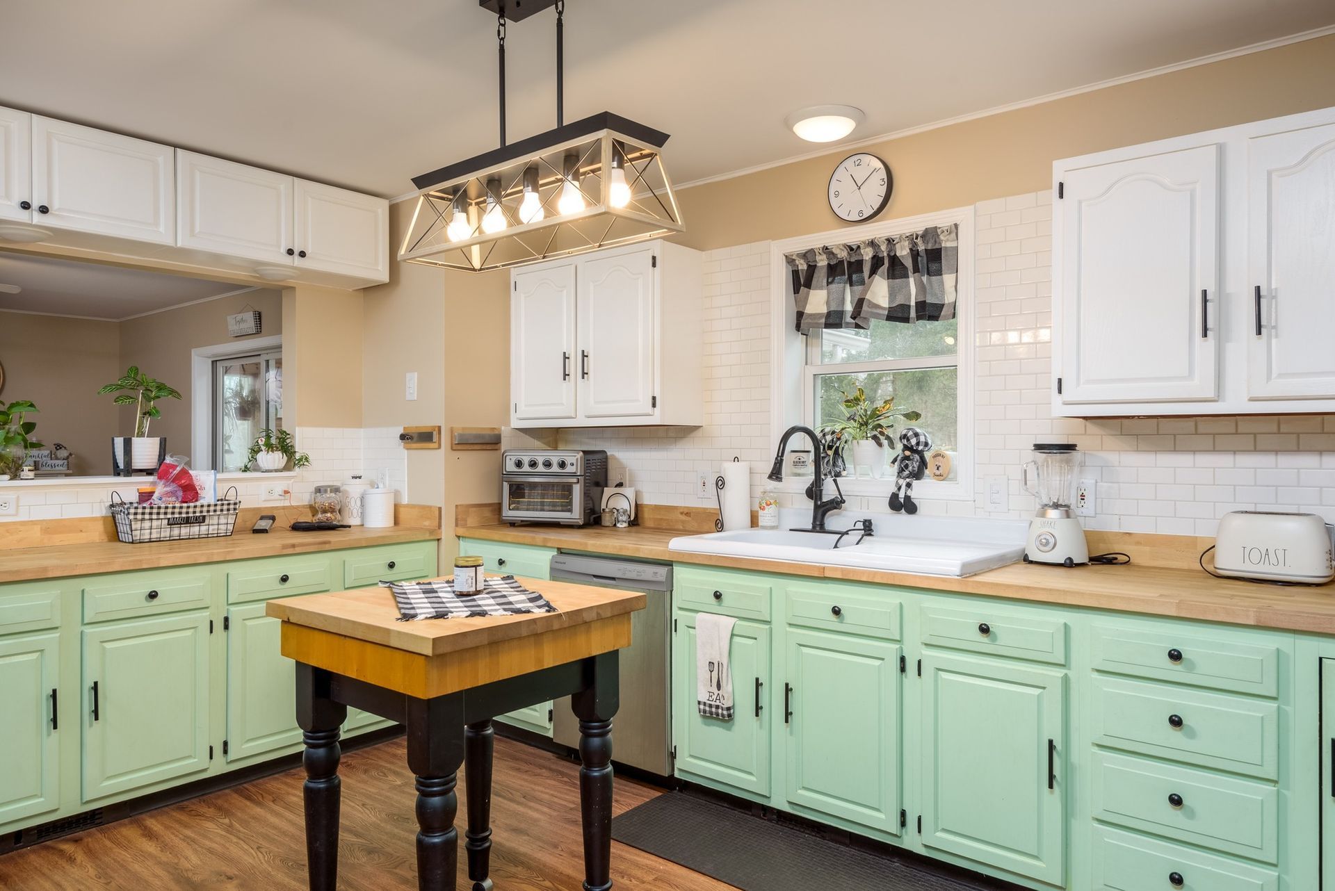 A kitchen with green cabinets , white cabinets and a wooden table.