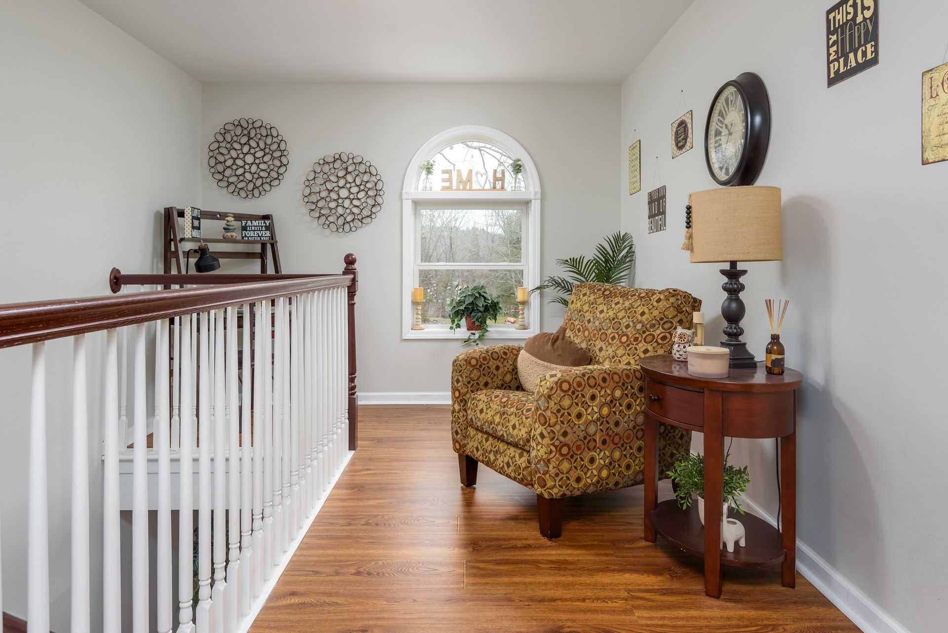 A living room with a chair , table , lamp and a clock on the wall.