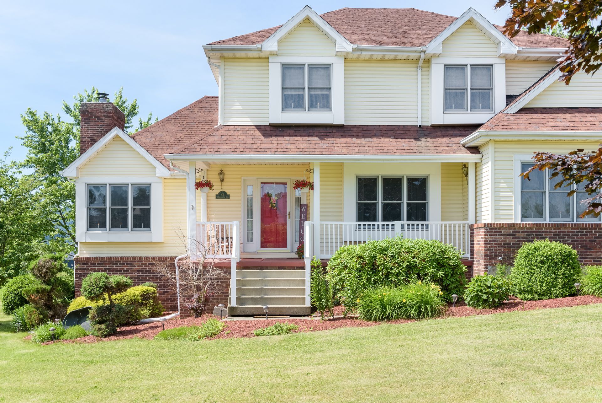 A large yellow house with a red door and a porch.