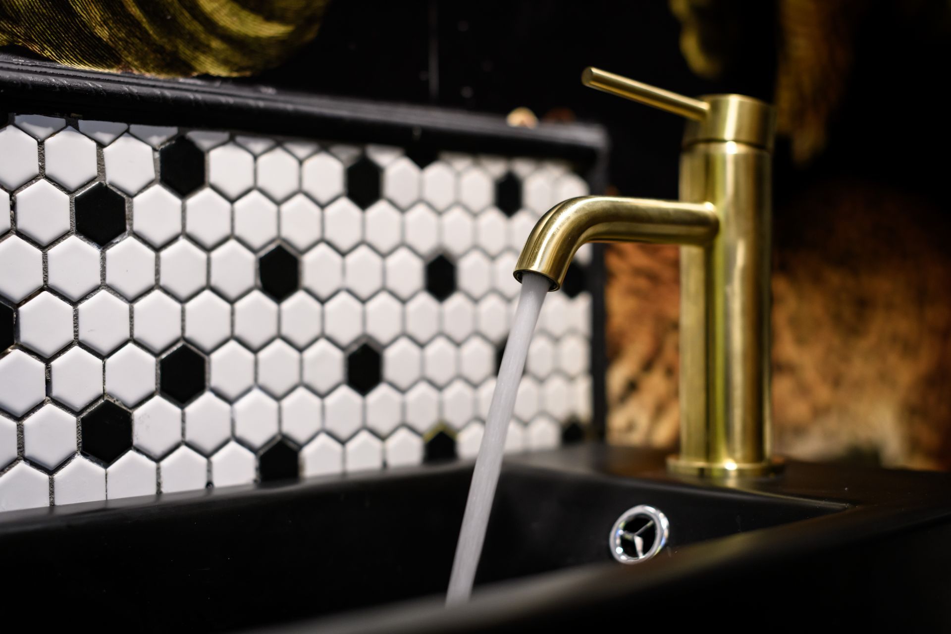 A bathroom sink with a gold faucet and black and white tiles.