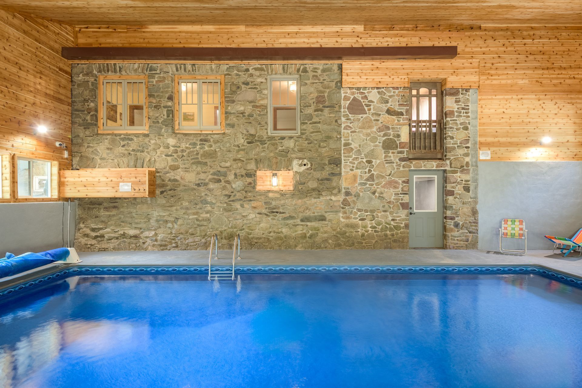 A large indoor swimming pool with a wooden ceiling and a stone wall.