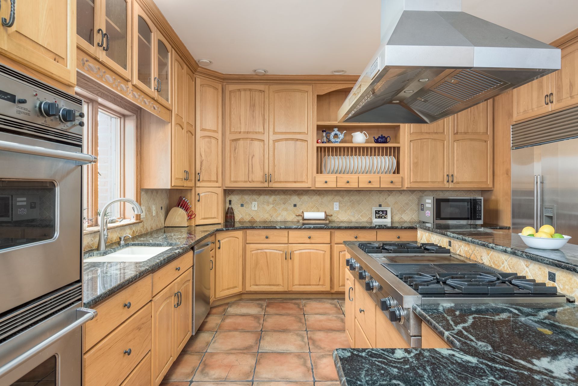 A kitchen with wooden cabinets , granite counter tops , stainless steel appliances and a stove.