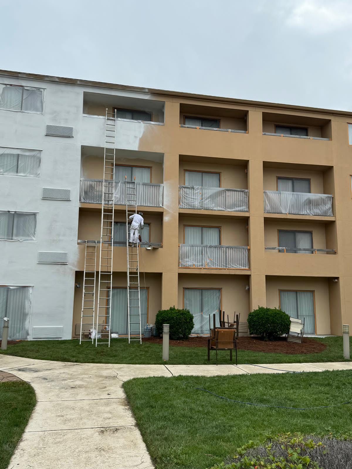 A person paints a building. The building is beige/white with balconies.