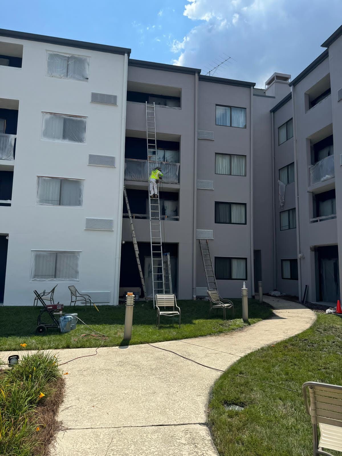 Exterior of an apartment building being painted. A person on a ladder is working.
