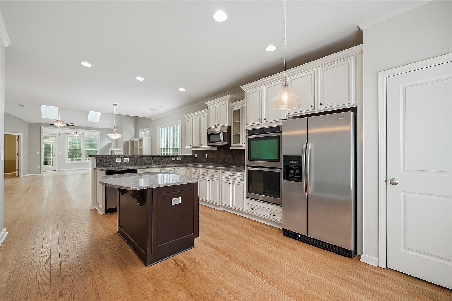 Kitchen with white cabinets, stainless steel appliances, dark island, and wood floors.